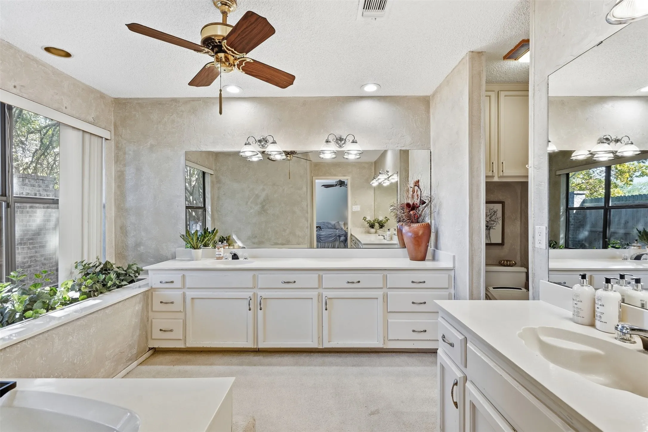 Dual vanity with white cabinetry and integrated sinks, extensive mirror, recessed lighting, and a ceiling fan