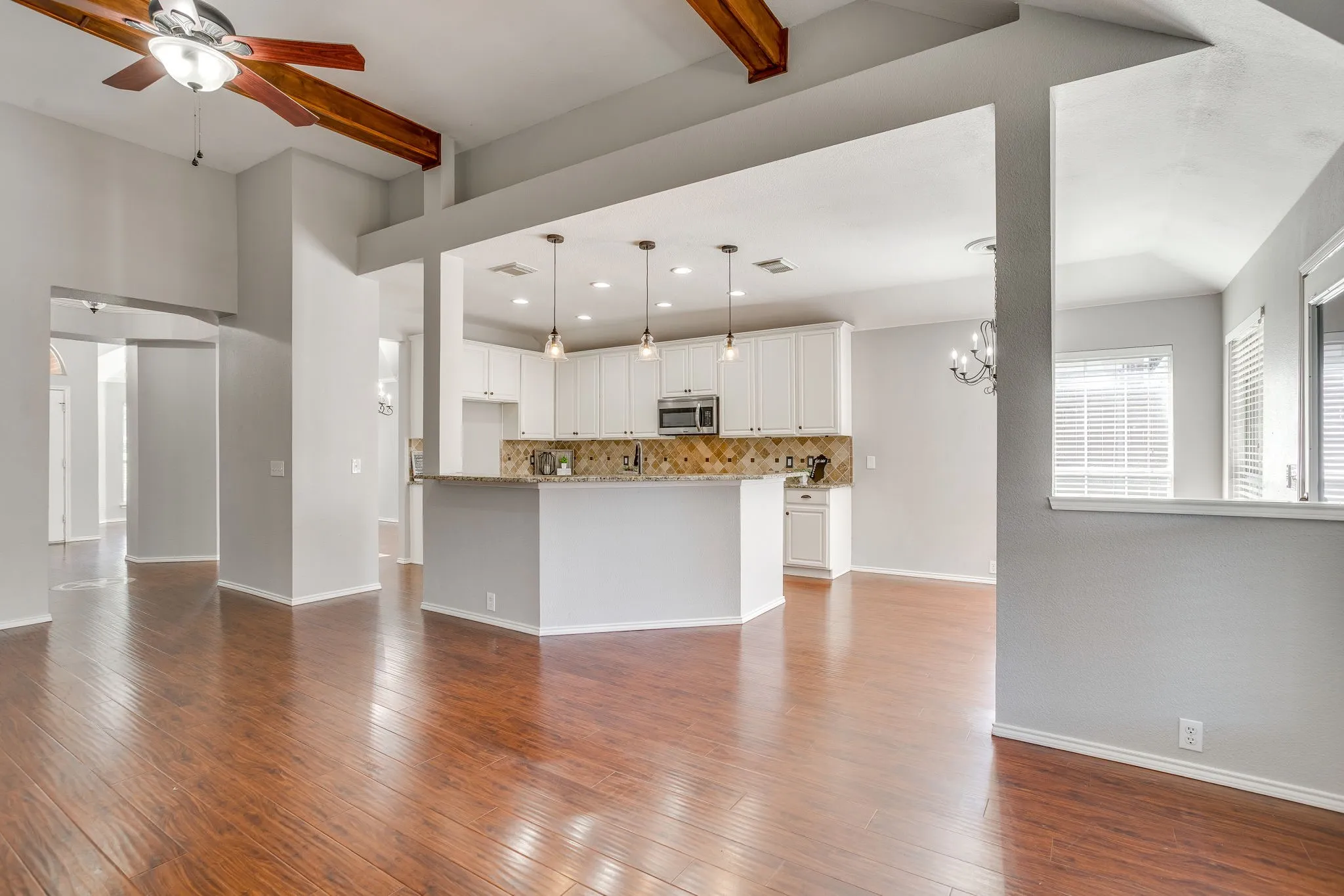 Vaulted ceiling with wood beams, wood-finish flooring, white kitchen cabinetry, stainless steel microwave, and pendant lighting