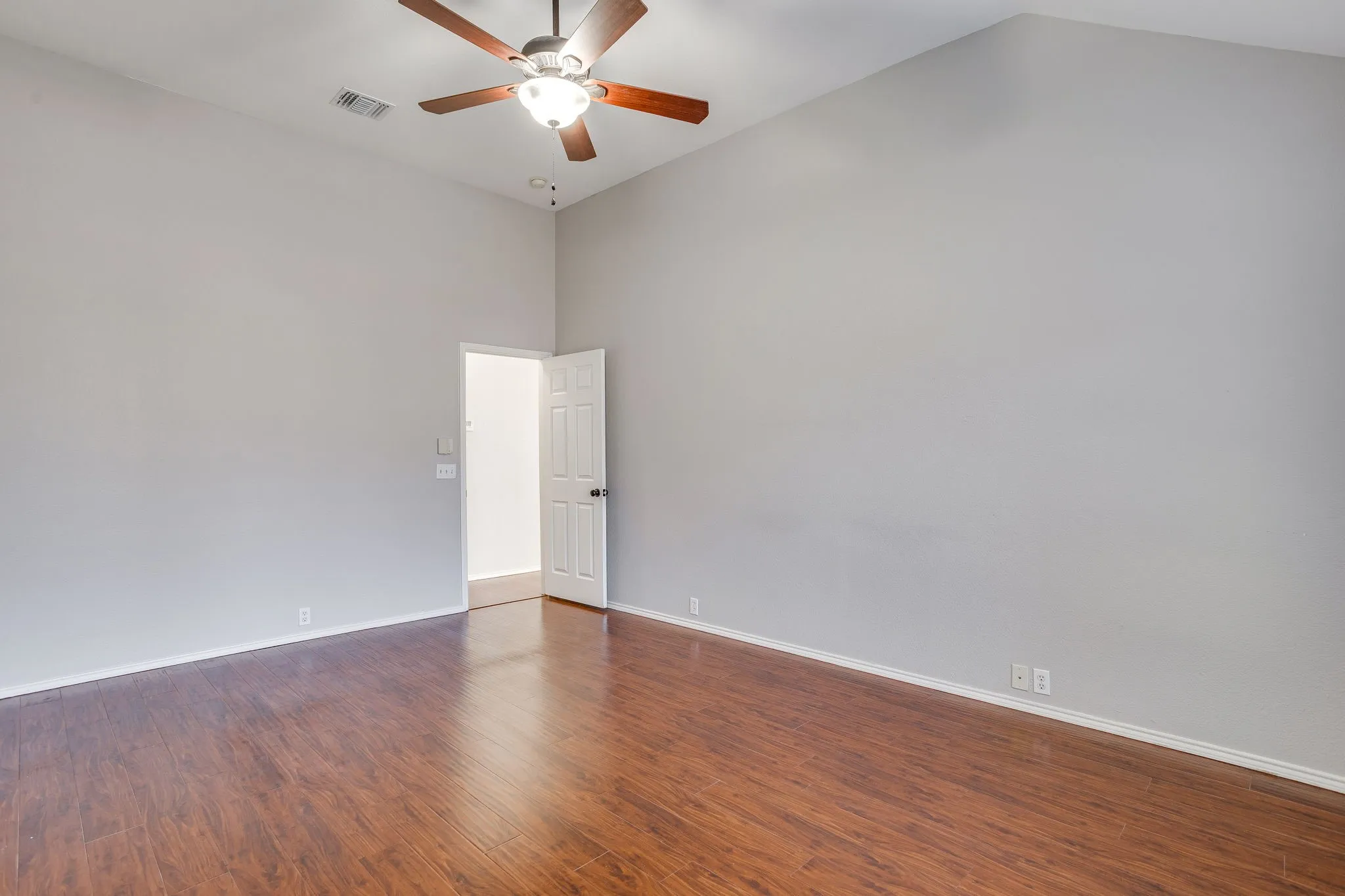 Vaulted ceiling with an integrated ceiling fan, wood-finish flooring, and light-toned wall paint