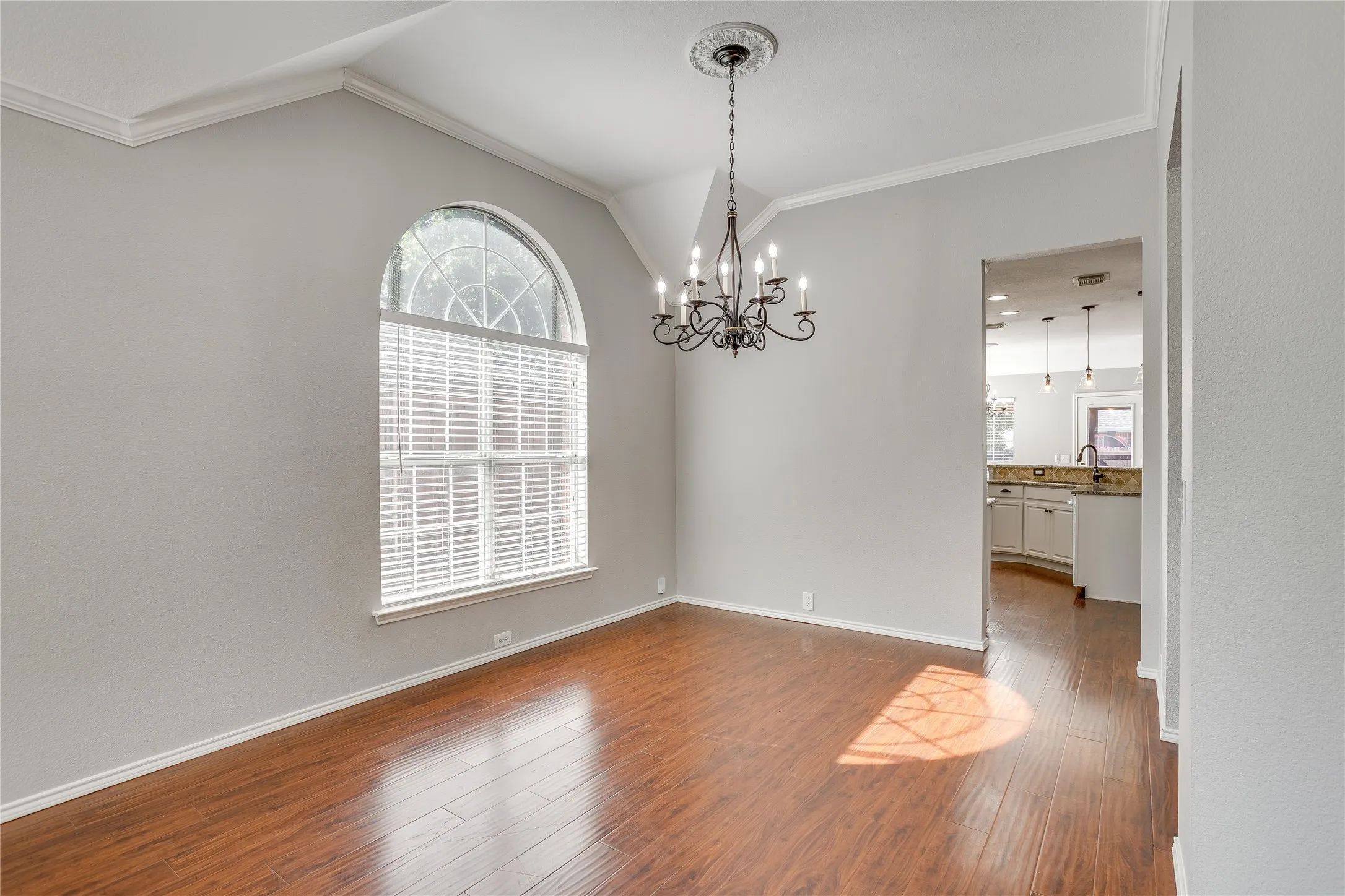 Arched window with blinds, wood-finish flooring, crown molding, and an ornate chandelier with ceiling medallion