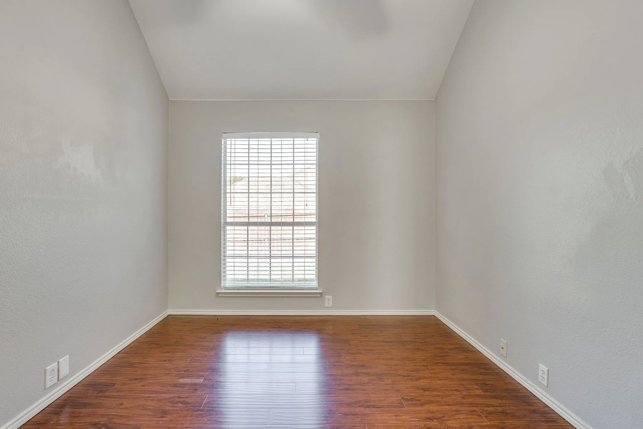 Wood-finish flooring with white trim, light-toned walls, and a window with blinds