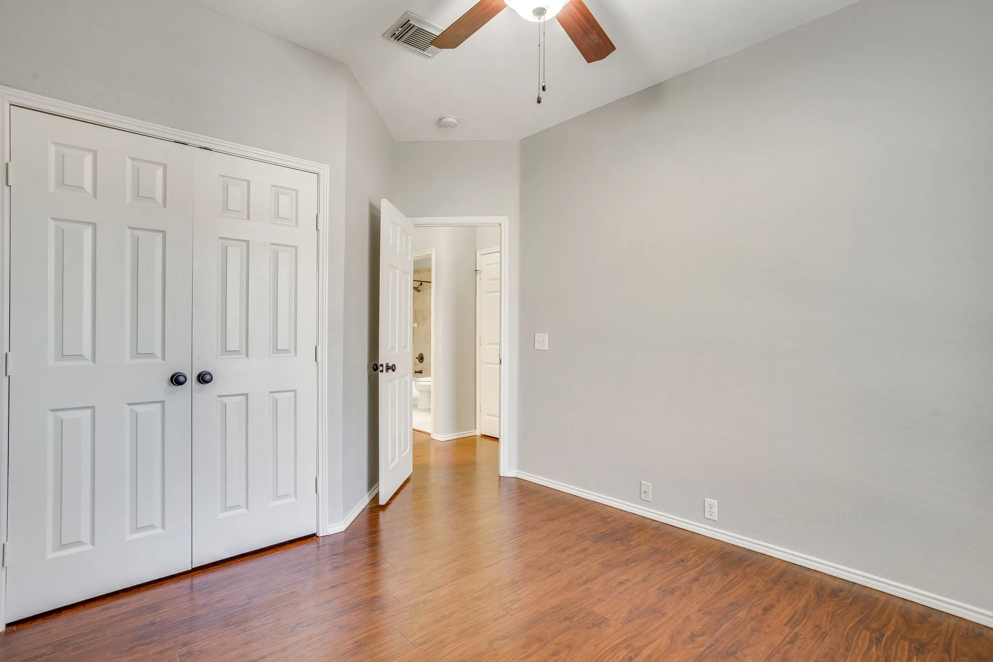 Wood-finish flooring throughout, bright white walls, and a ceiling fan with integrated lighting