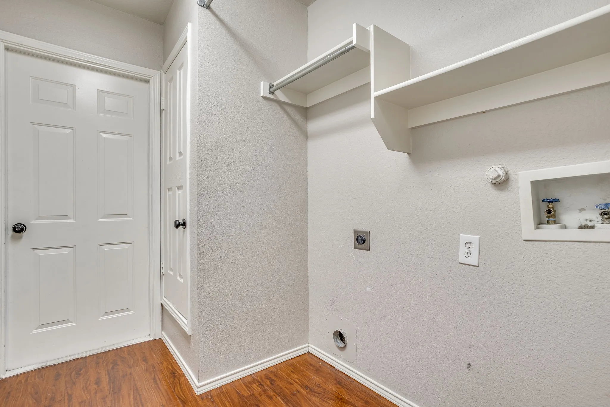 Dedicated utility space featuring wood-finish flooring, built-in shelving, and a hanging rod