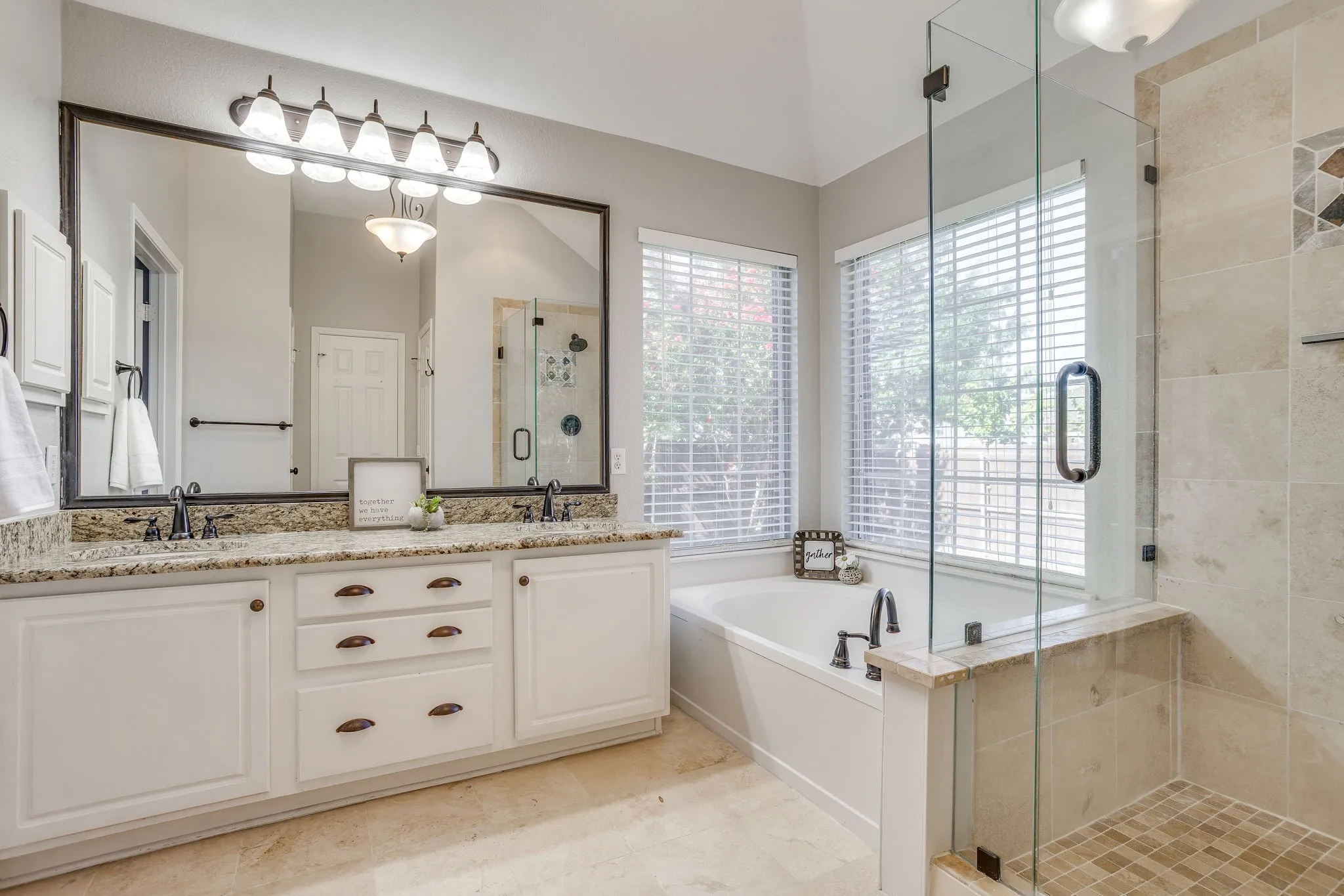 Dual vanity with granite countertop, white cabinetry, and bronzed hardware