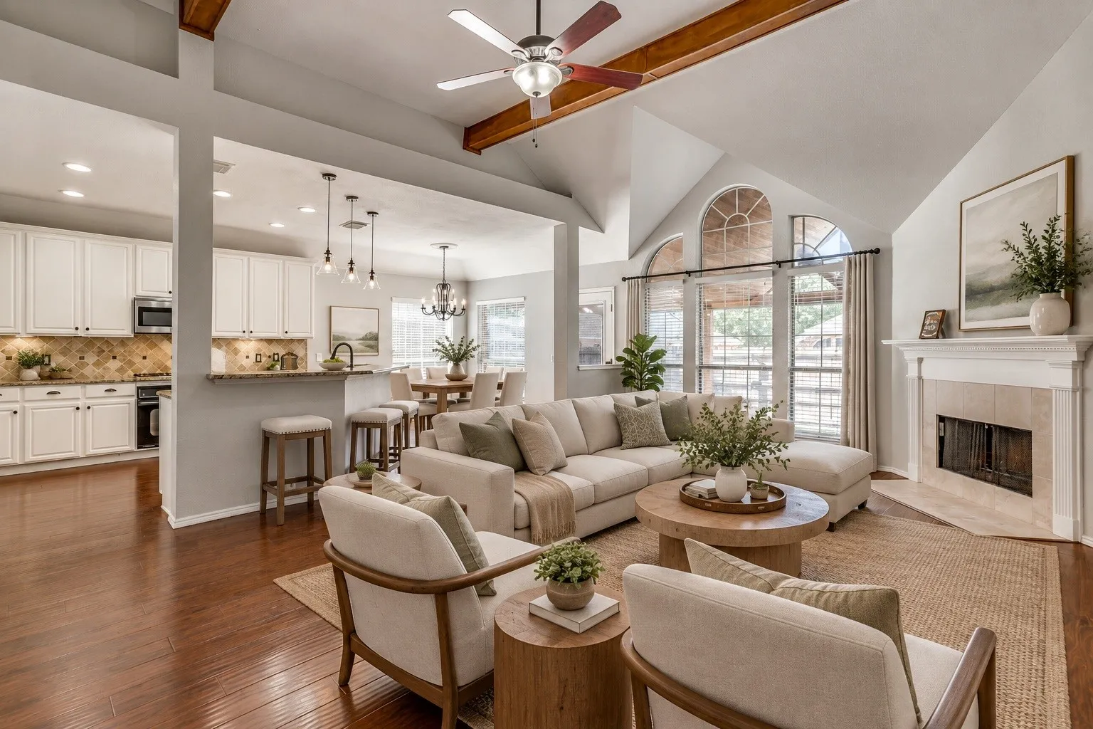 Vaulted ceilings with exposed beams, fireplace with a mantle, large arched windows, wood-finish flooring, and a kitchen with white cabinetry. This photo was virtually staged using AI.