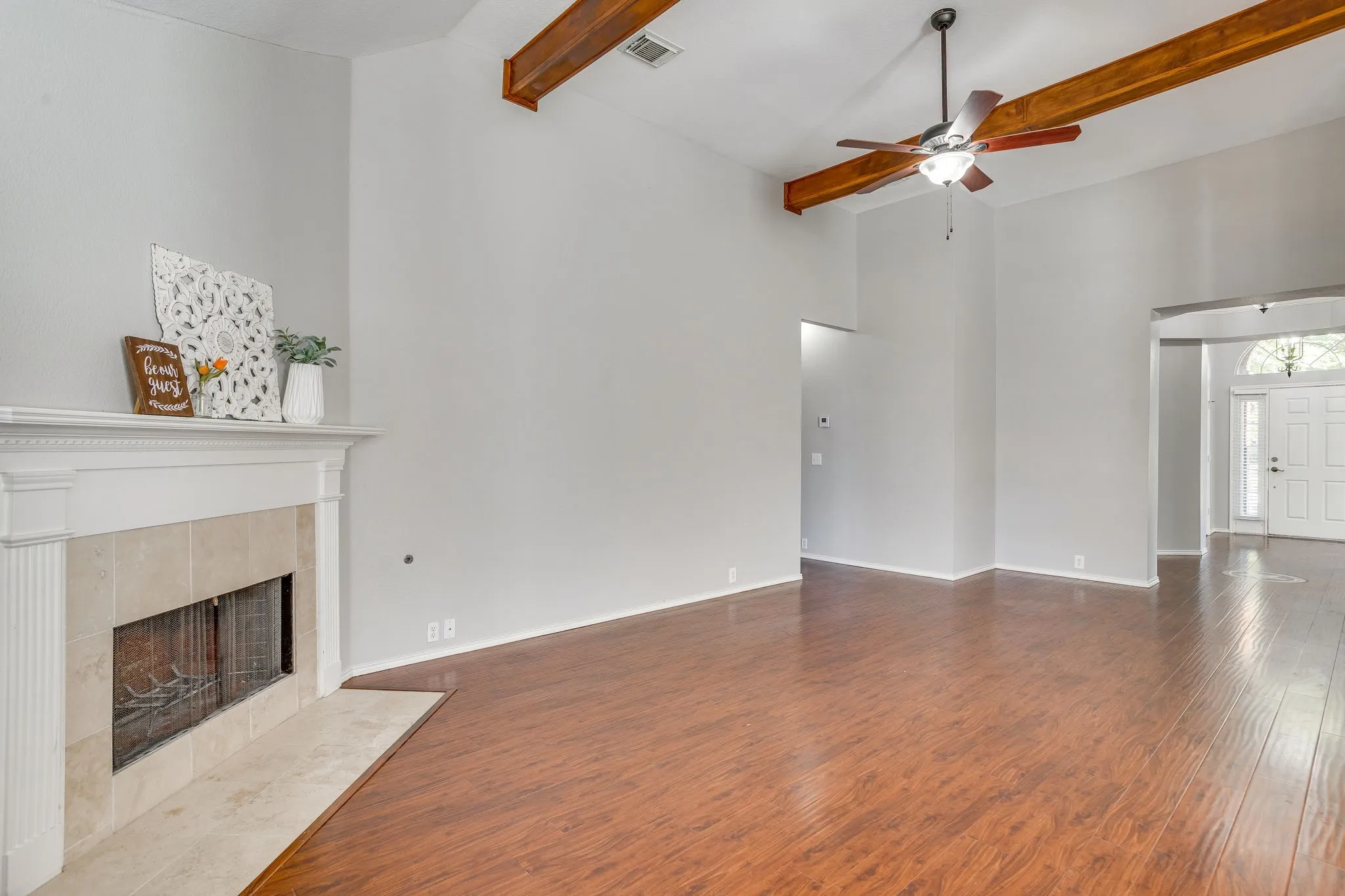 Vaulted ceilings with exposed wood beams, wood-finish flooring, and a fireplace featuring a white mantel and stone surround