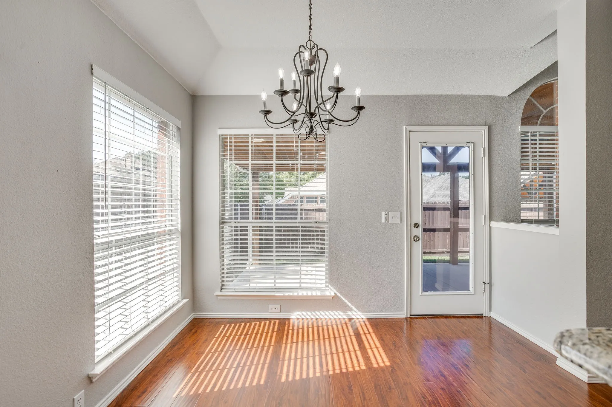 Vaulted ceiling, wood-finish flooring, multiple windows with blinds, arched window, and a glass-paneled exterior door