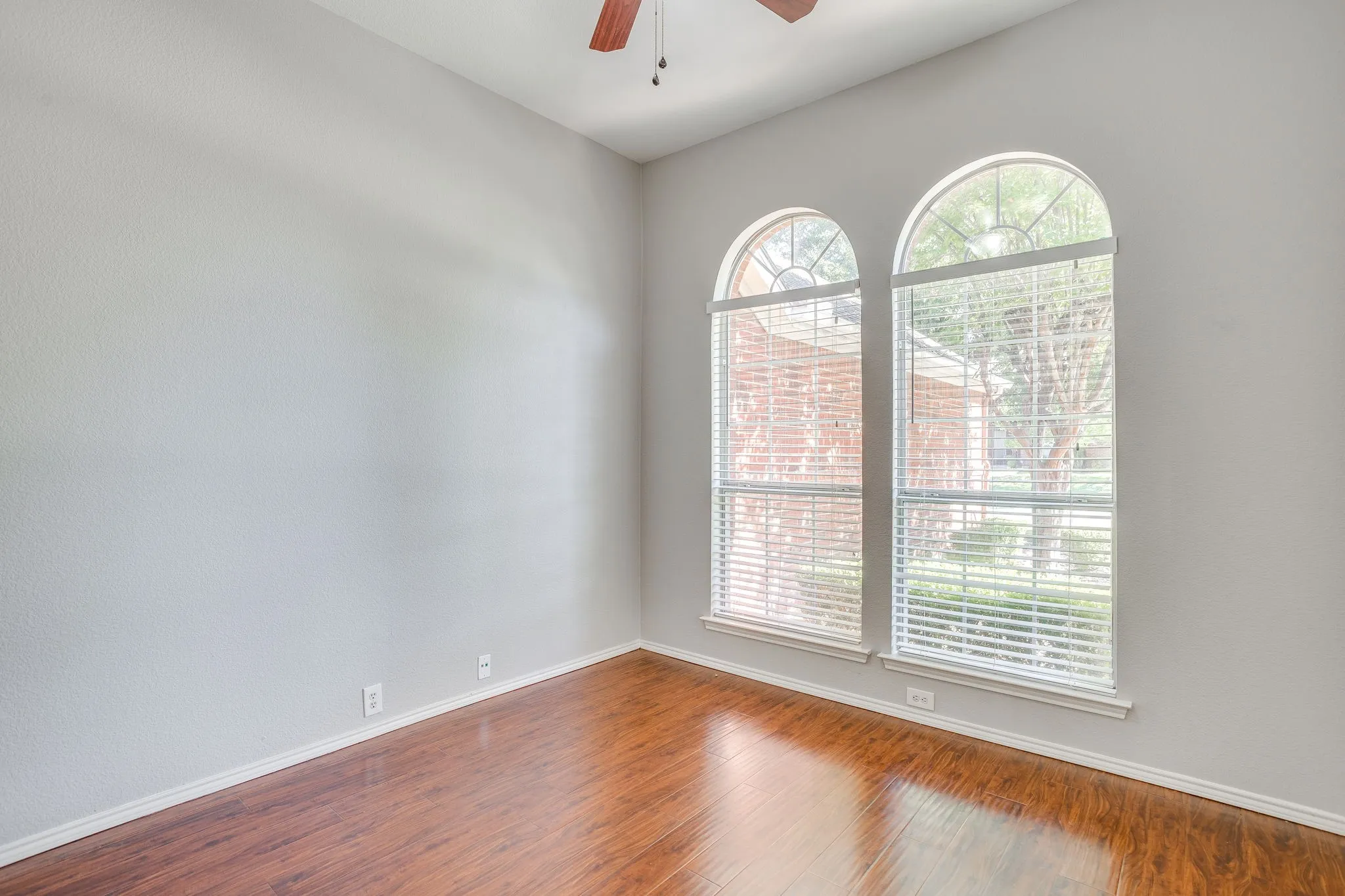 Arched windows with blinds, wood-finish flooring, vaulted ceiling, and a ceiling fan