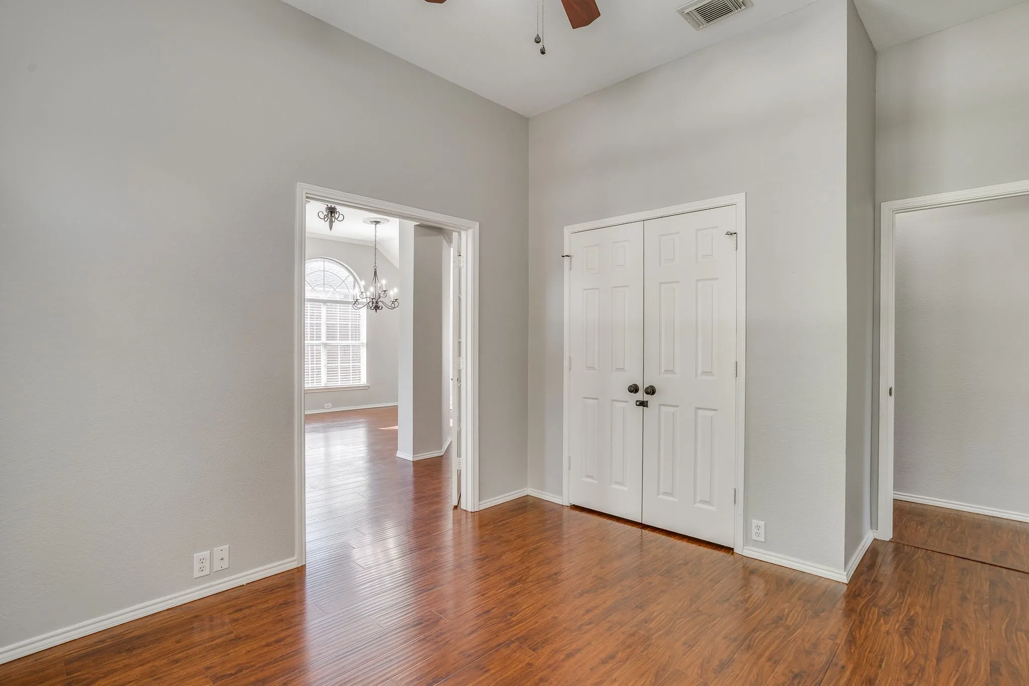 Wood-finish flooring, white paneled doors, ceiling fan with light fixture, and arched window in background