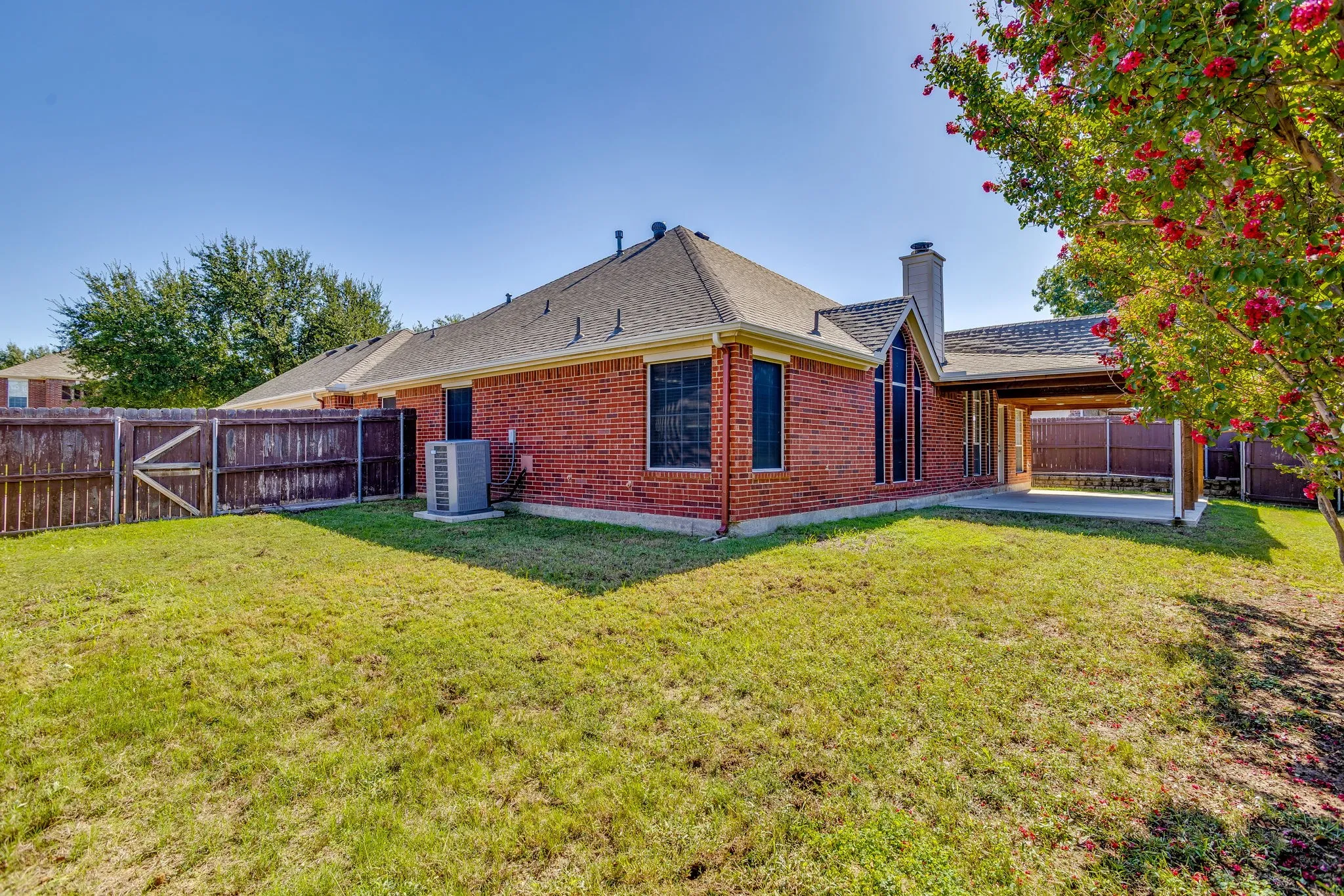 Expansive lawn area with a wood privacy fence, brick exterior, covered patio, and a prominent chimney