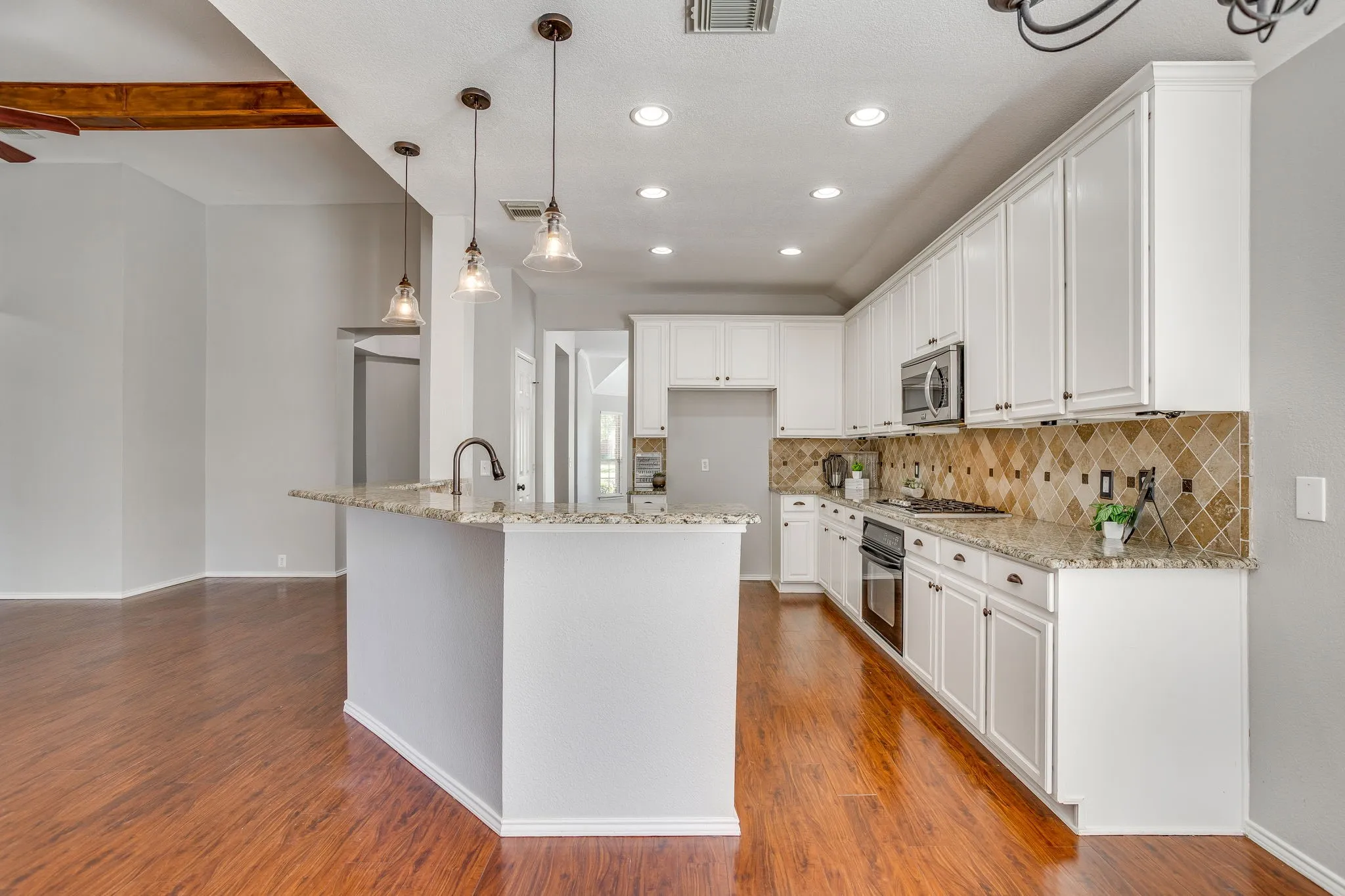 Kitchen with wood-finish flooring, white cabinetry, integrated stainless steel appliances, and a tiled backsplash