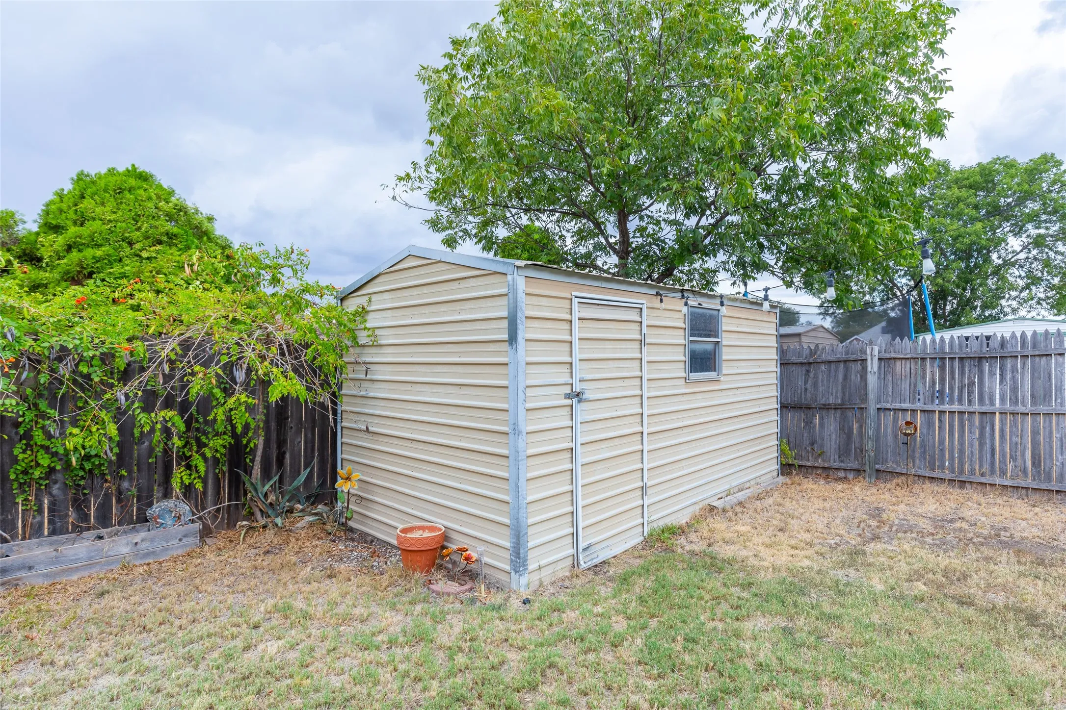 Freestanding storage shed with corrugated metal siding, a single window, and a wood privacy fence
