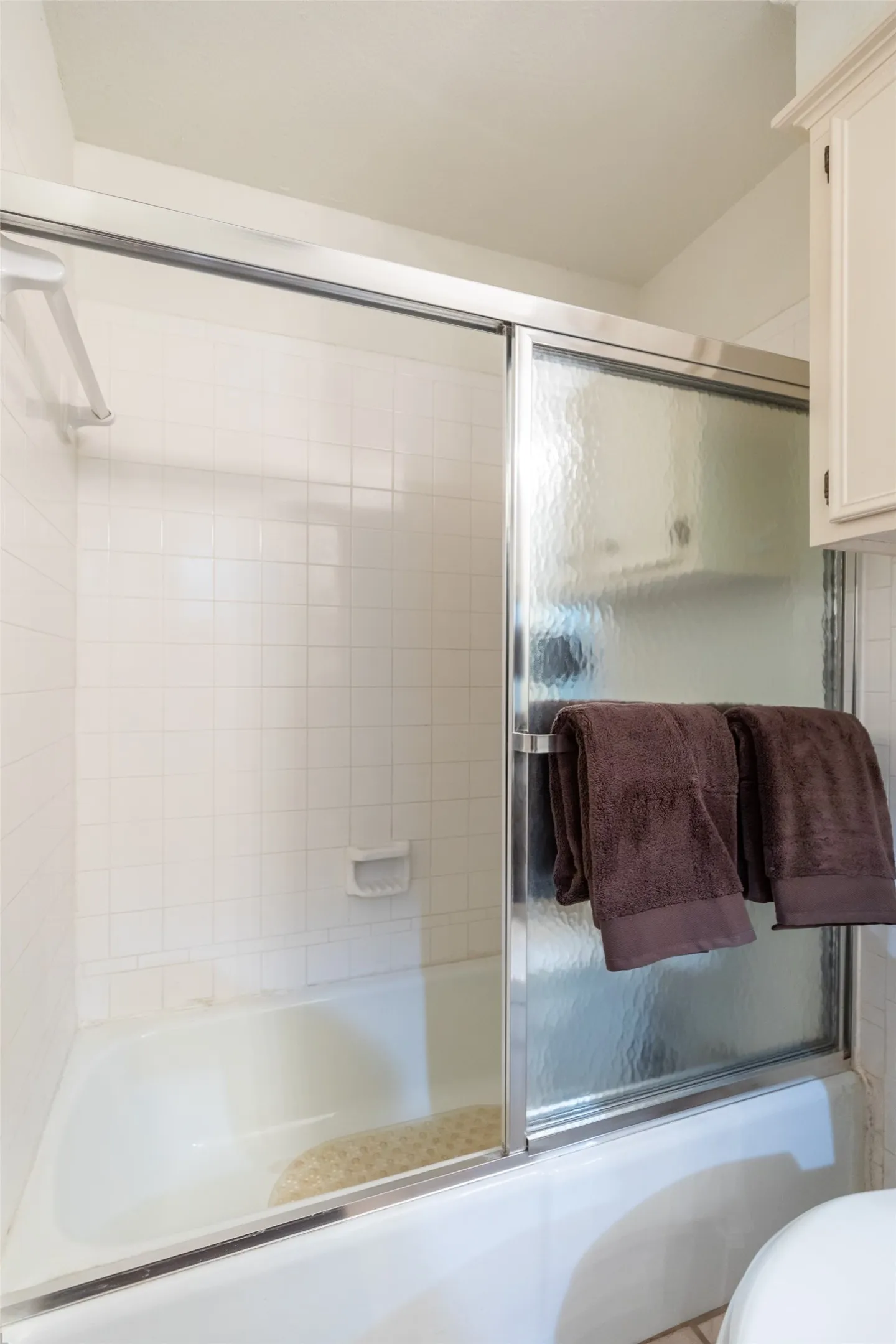 Bathtub with white tile surround and sliding glass shower doors