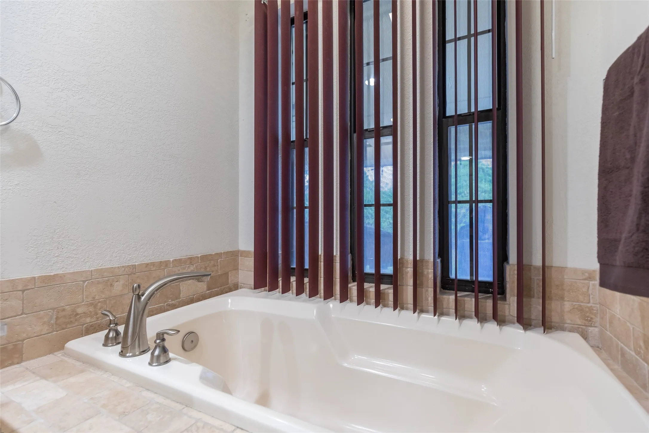 Built-in soaking tub with a brushed nickel faucet, surrounded by tiled decking and wainscoting