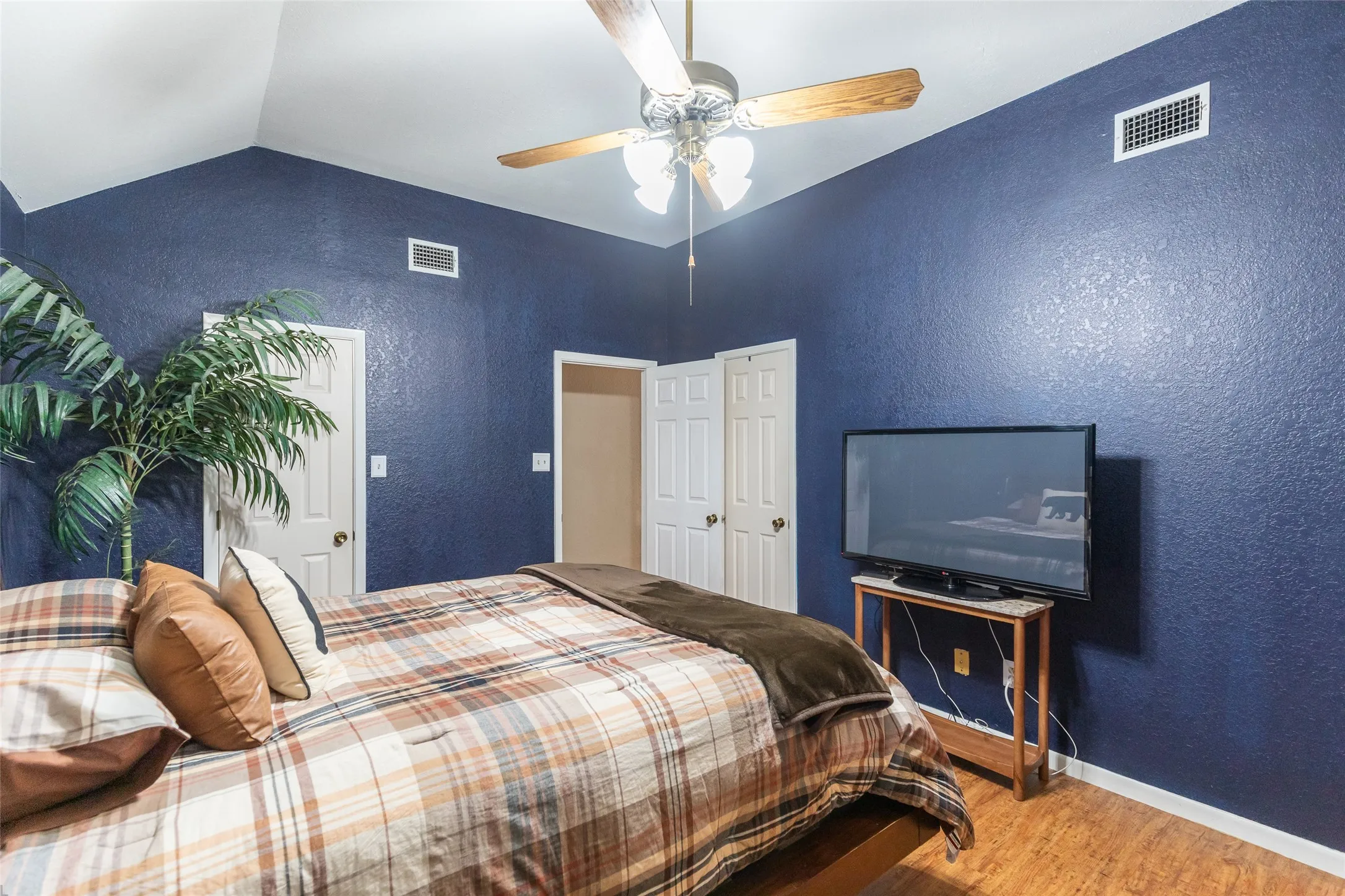 Vaulted ceiling with a wood-blade ceiling fan, wood-finish flooring, and white paneled doors