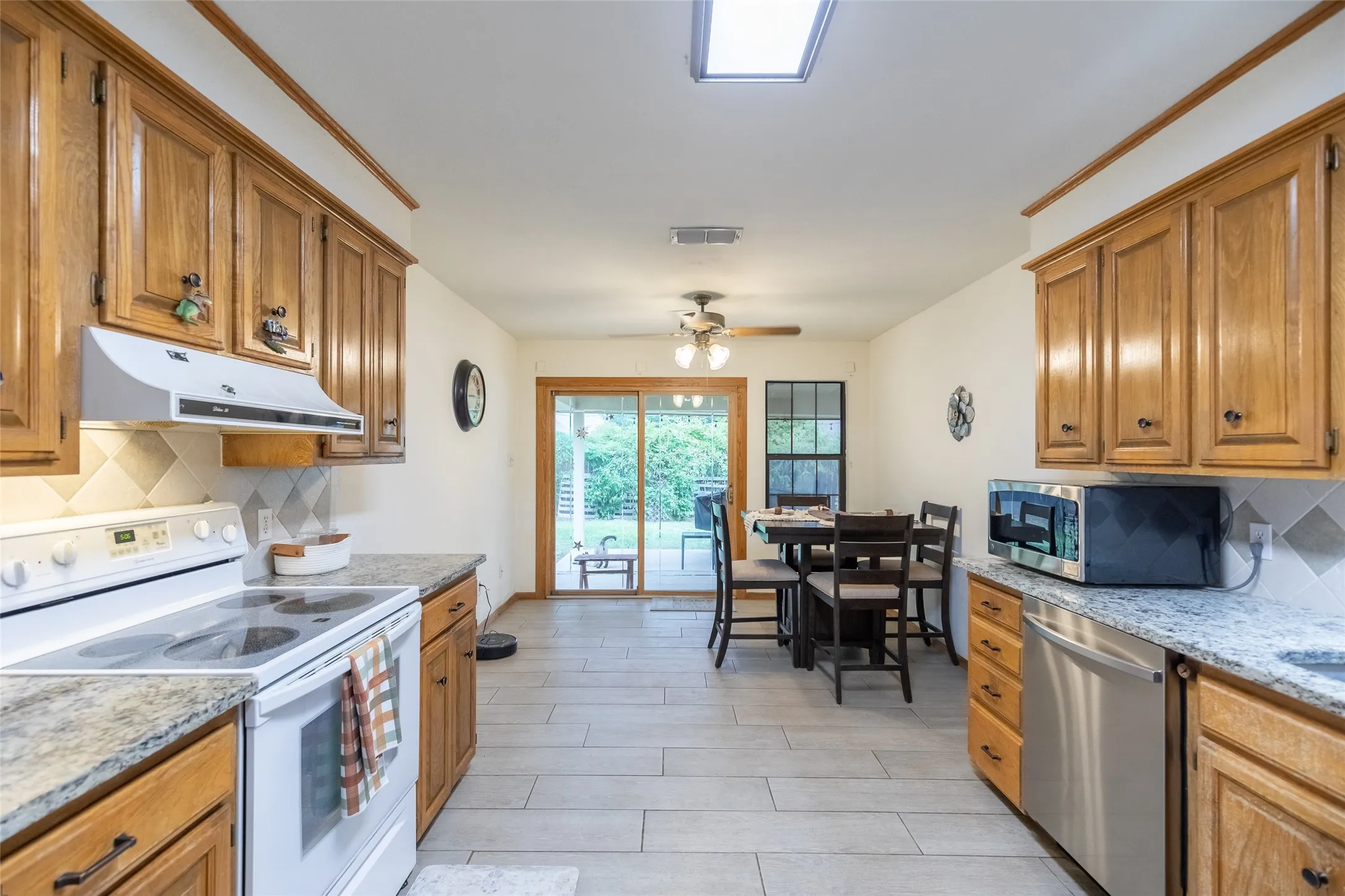 Kitchen featuring wood cabinetry, light-toned countertops, a tile backsplash, and light-toned tile flooring