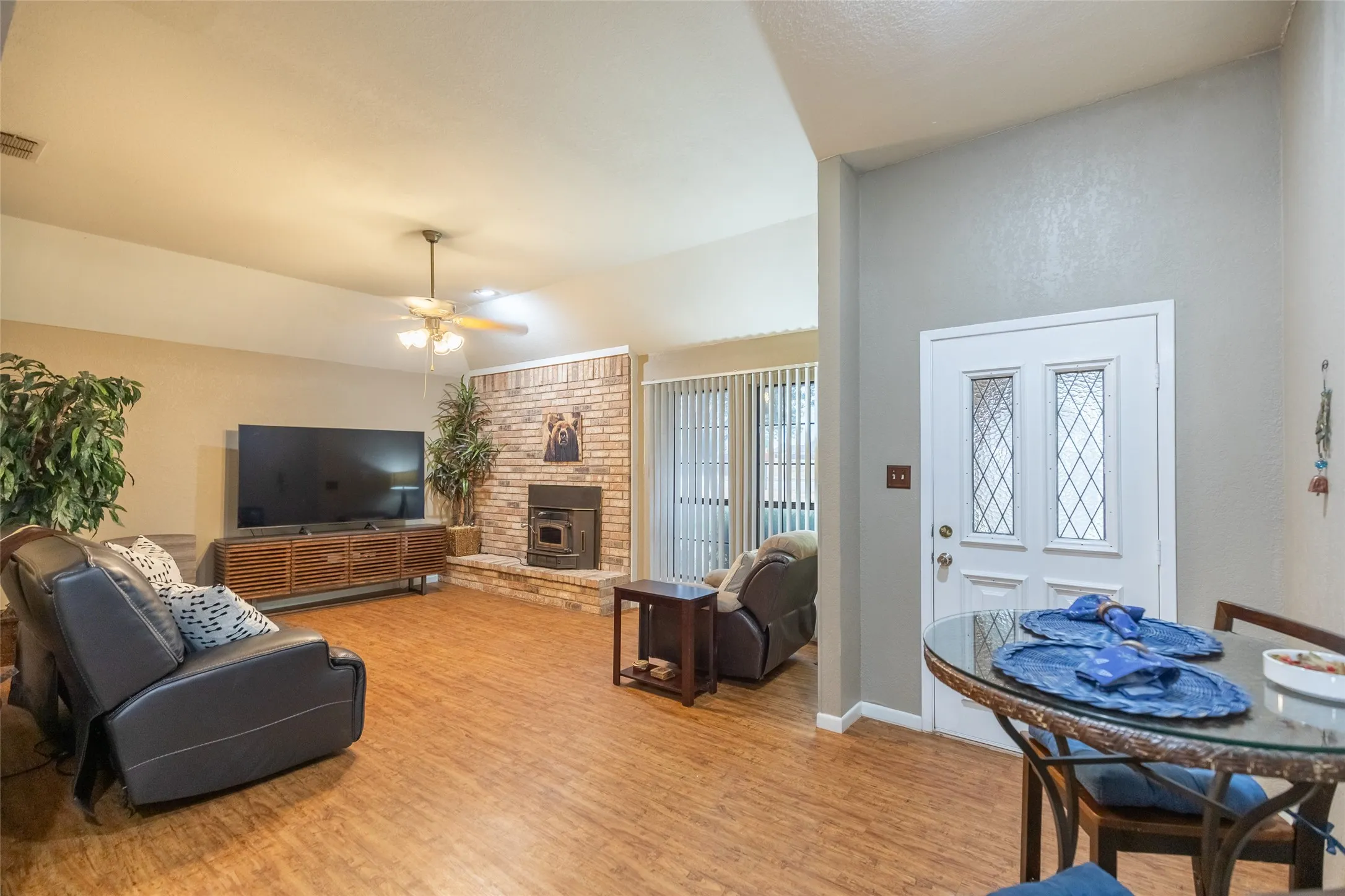 Spacious living area featuring wood-finish flooring, a brick fireplace with a hearth, and a ceiling fan