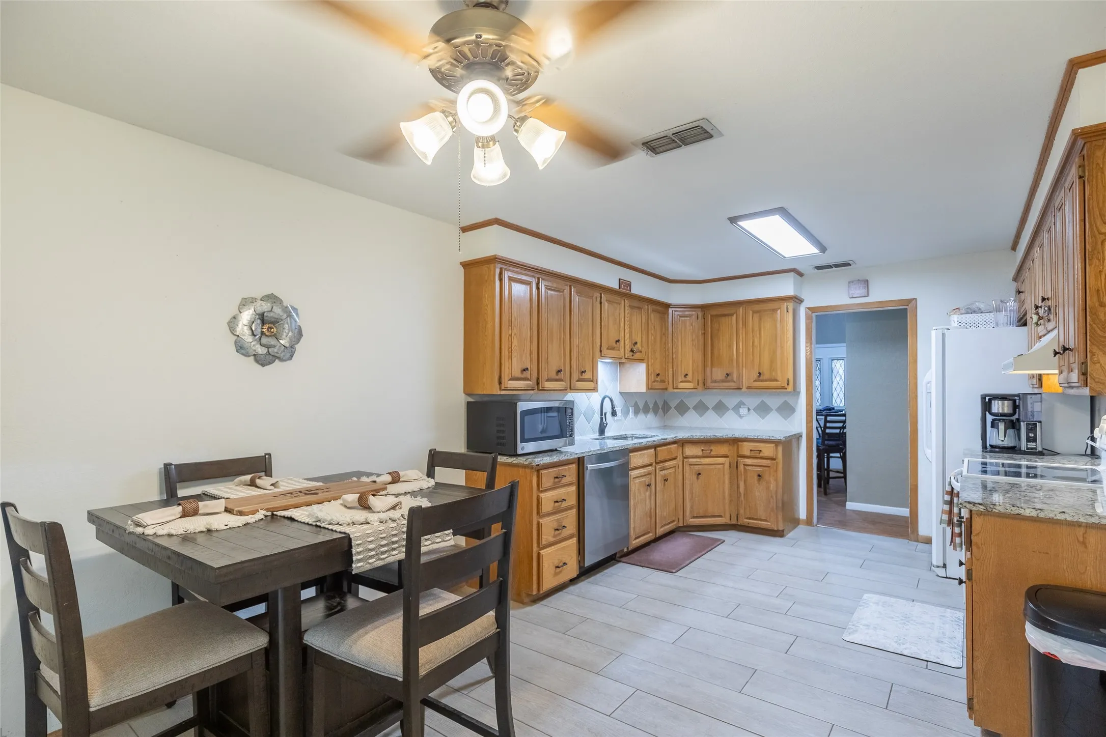 Kitchen featuring wood cabinetry, stainless steel dishwasher, tile backsplash, granite countertops, and light-toned tile flooring