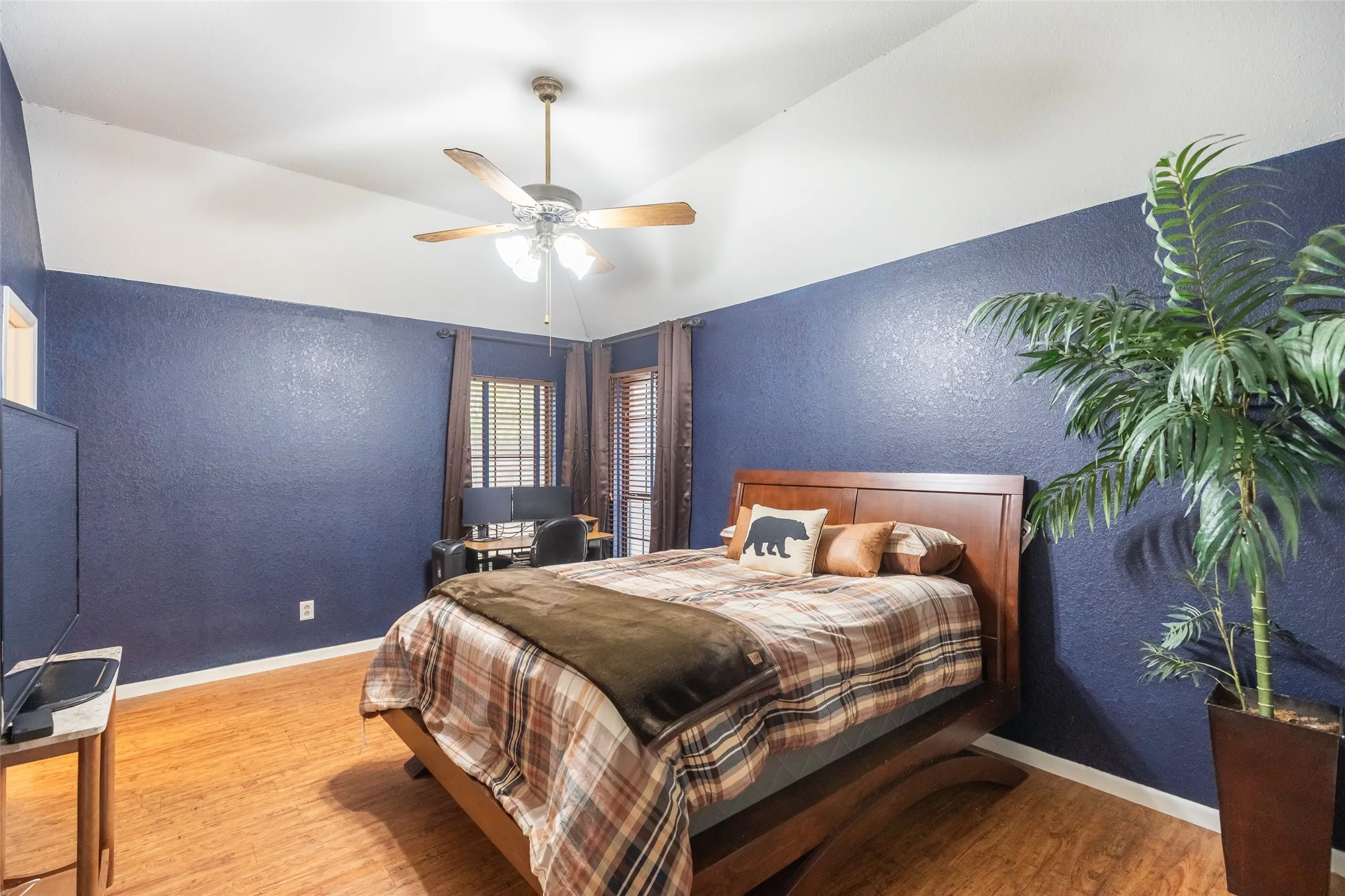 Vaulted ceiling featuring a ceiling fan, wood-finish flooring, and window treatments