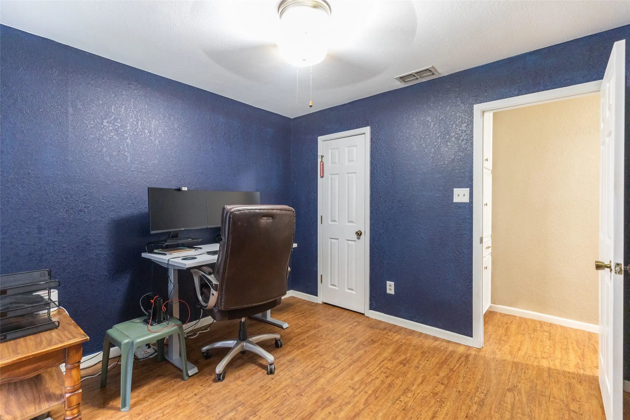 Wood-finish flooring with a textured ceiling, a ceiling-mounted light fixture, and a paneled door