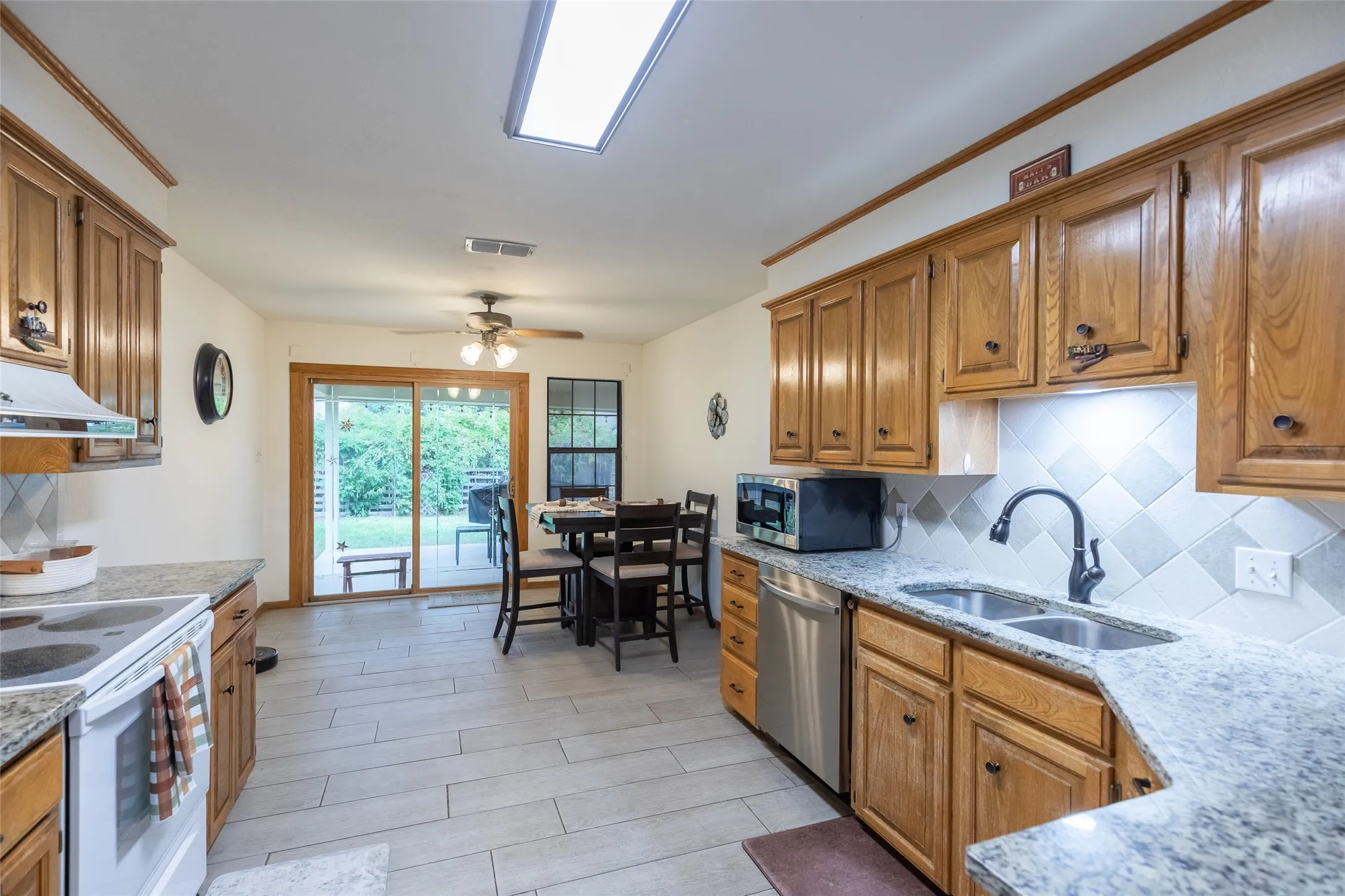 Kitchen featuring granite countertops, wood cabinetry, stainless steel dishwasher, tile flooring, and a sliding glass door to the exterior
