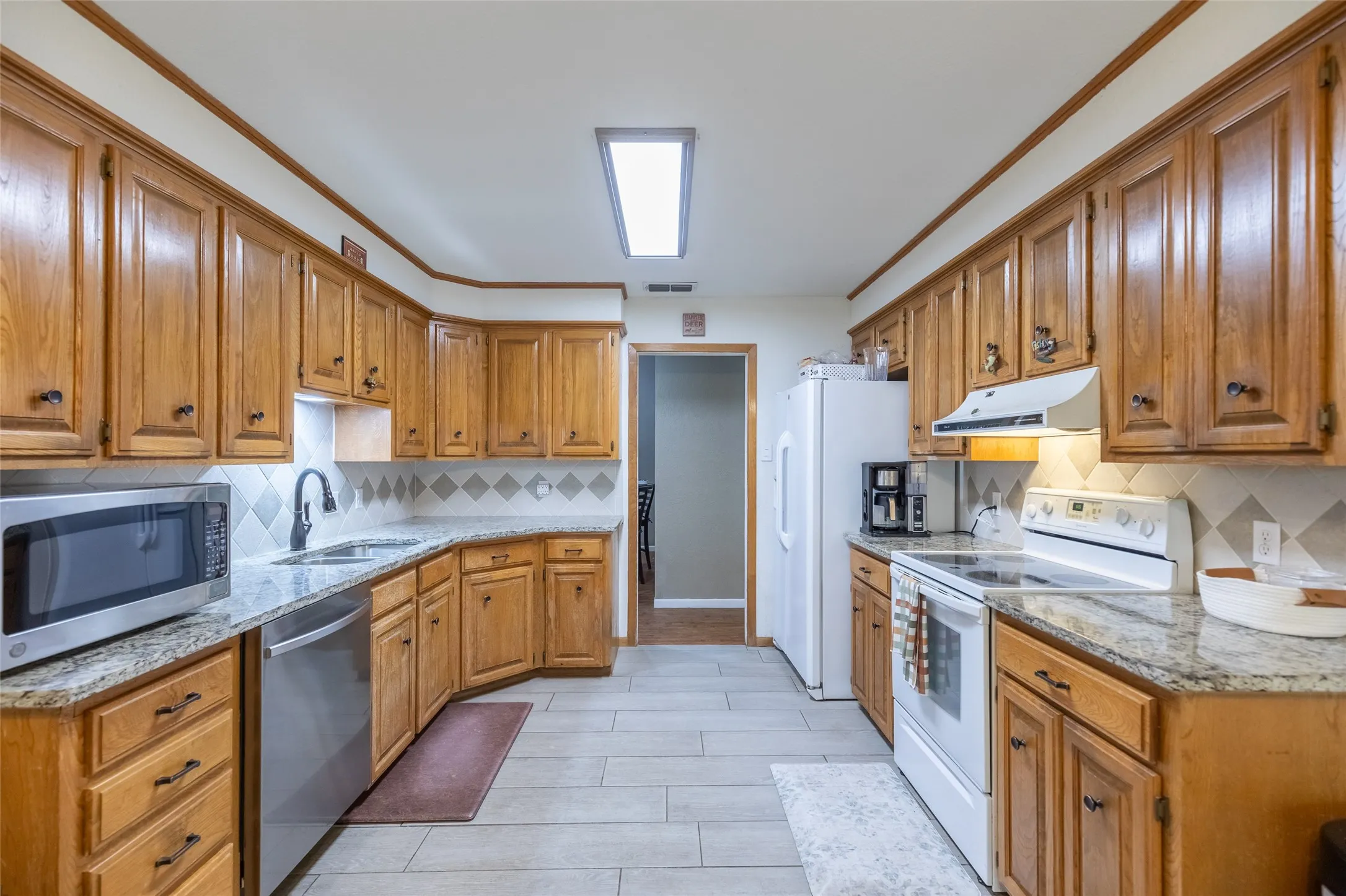 Kitchen featuring honey-toned wood cabinetry, stone countertops, a stainless steel sink, tile backsplash, and light-toned tile flooring