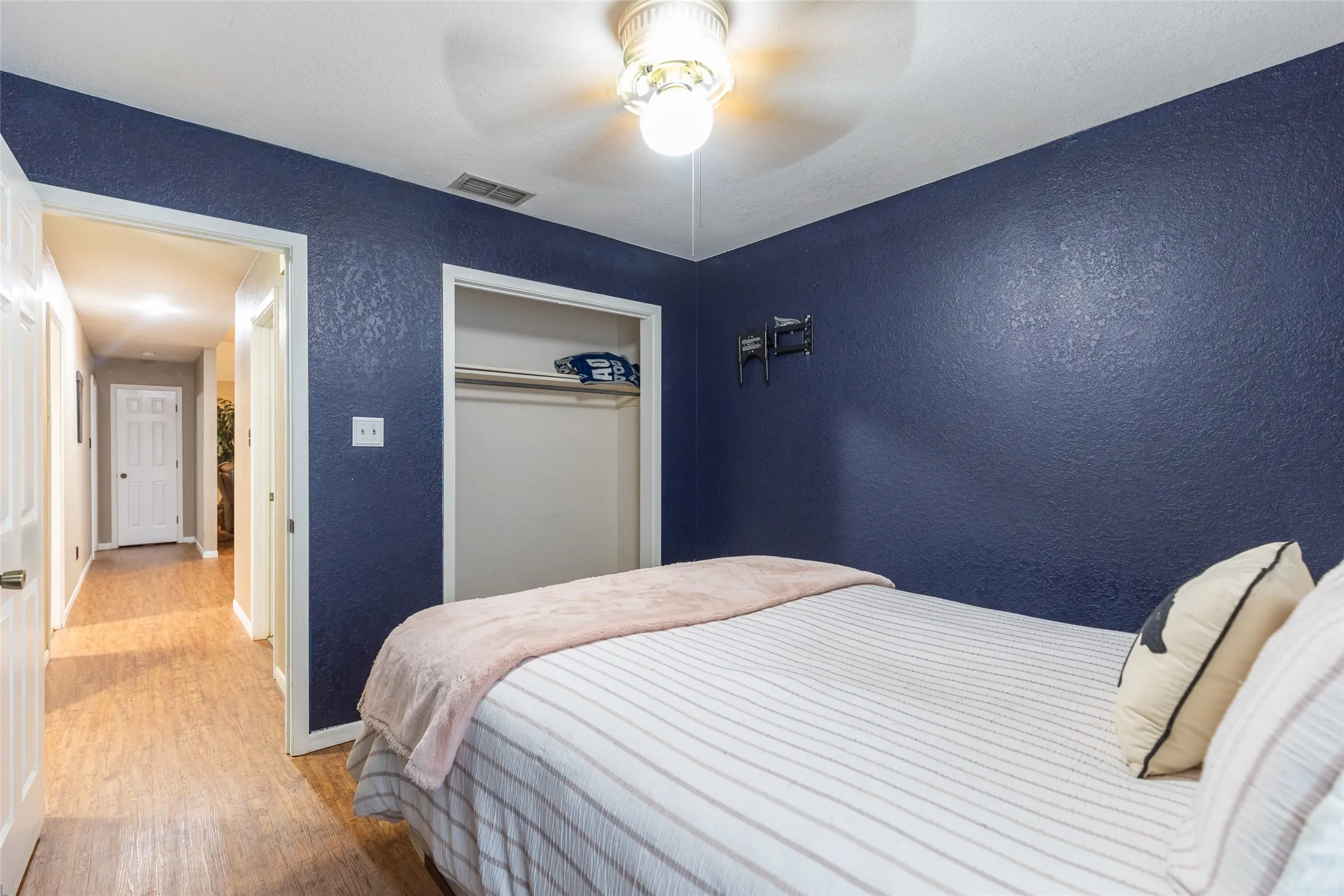 Bedroom with wood-finish flooring, a built-in closet with shelving, and a ceiling fan with integrated lighting
