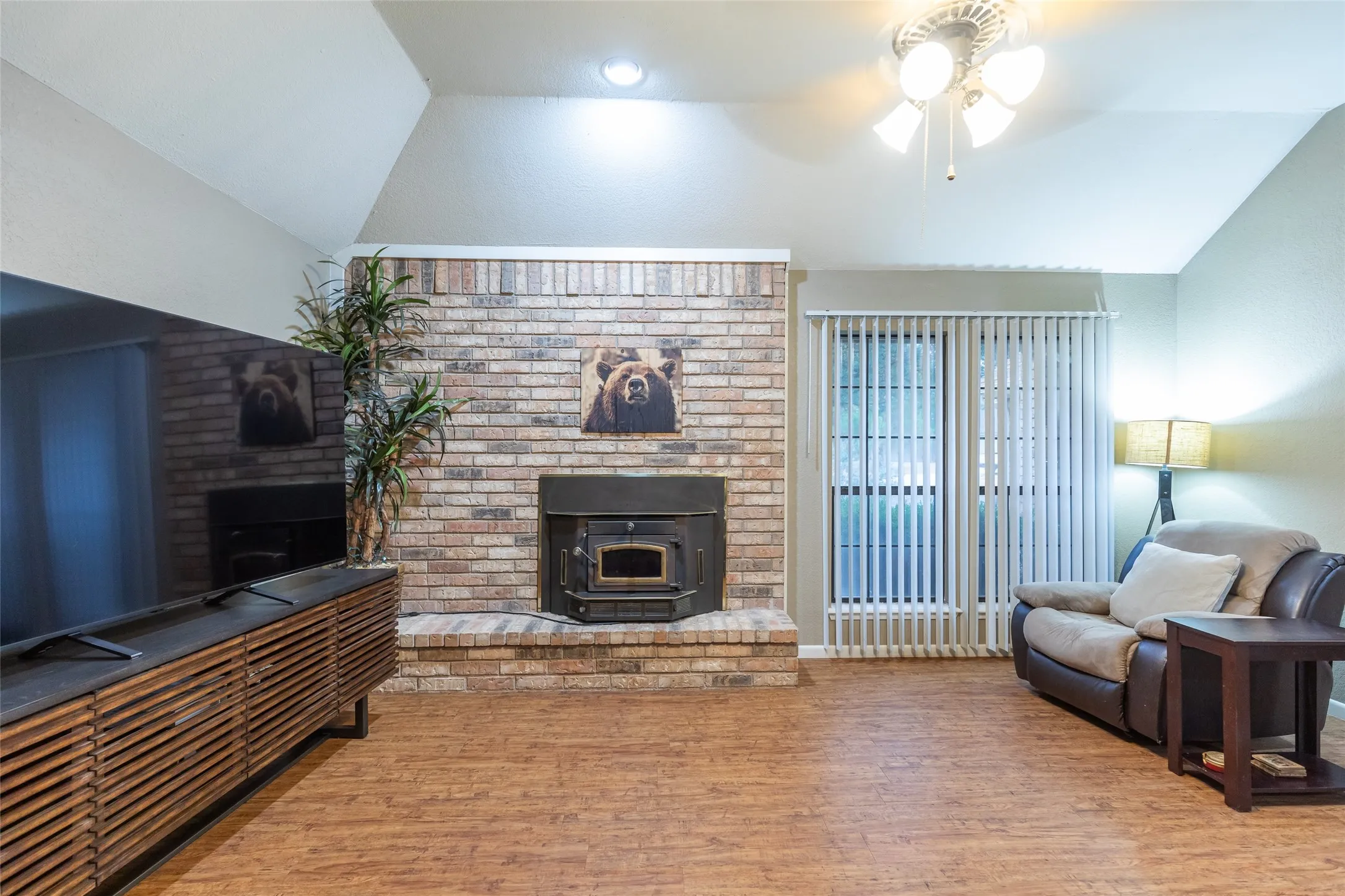 Brick-faced fireplace with hearth, wood-finish flooring, vaulted ceiling, and sliding glass door