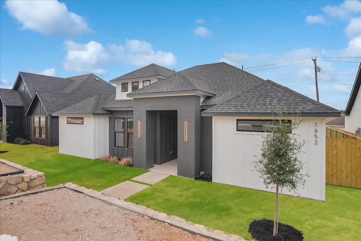 Contemporary exterior with a covered entry, dark grey brick, white vertical siding, and a gabled roofline