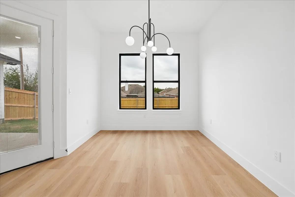 Wood-finish flooring throughout, bright white walls, modern chandelier, two black-framed windows, and a glass-paneled door