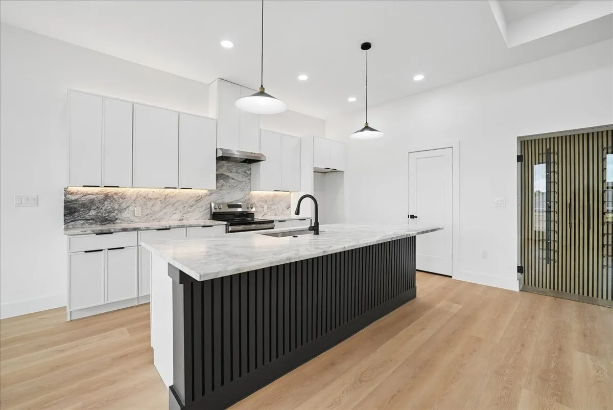 Bright kitchen featuring a central island with a stone countertop, white cabinetry with dark hardware, and light wood-finish flooring