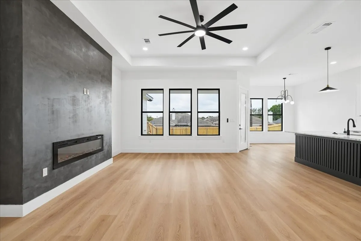 Wood-finish flooring throughout, modern wall-mounted fireplace, black framed windows, white walls, and a contemporary ceiling fan