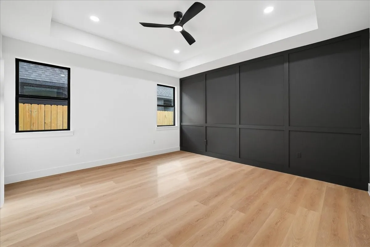 Recessed lighting, ceiling fan, tray ceiling, wood-finish flooring, and accent wall with paneling