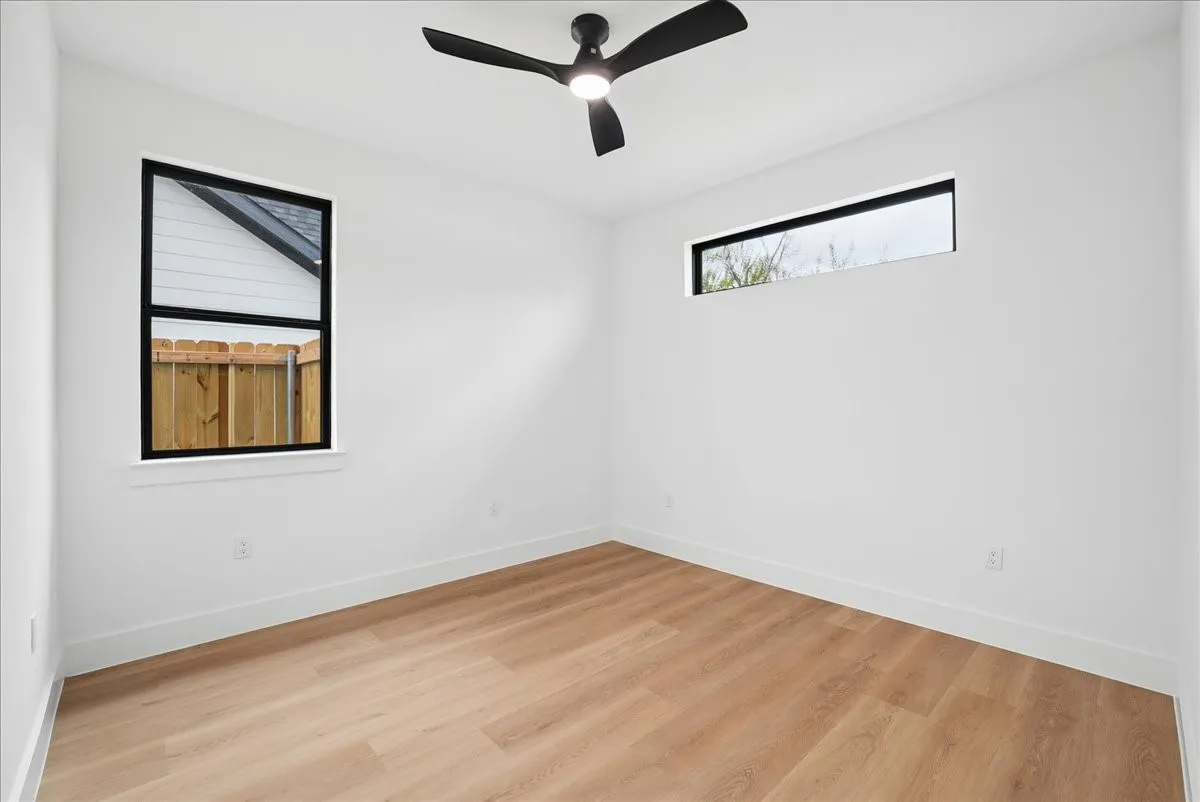 Light wood-finish flooring, two distinct window styles, and a contemporary ceiling fan with integrated lighting