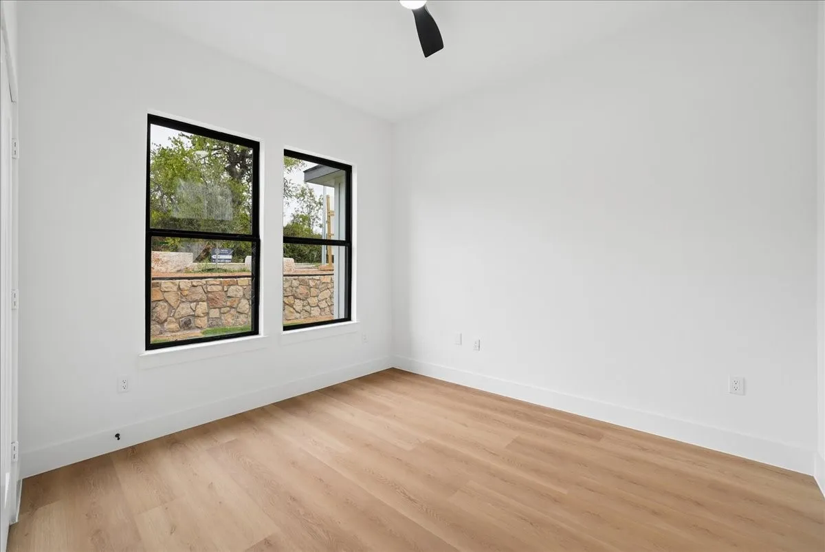 Bright interior with wood-finish flooring, two large windows, a ceiling fan, and white walls
