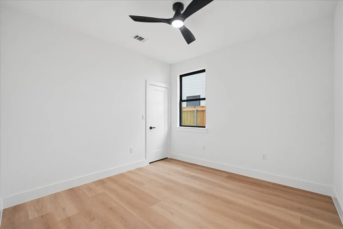 Neutral wall tones, wood-finish flooring, a modern black ceiling fan with integrated lighting, and a black-framed window