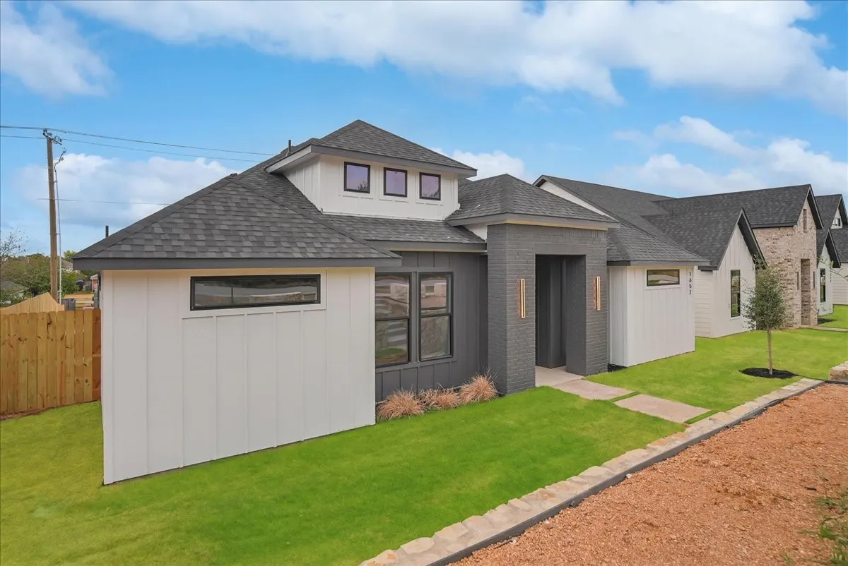 Contemporary home with mixed material exterior, dark gray brick accents, white vertical siding, dark shingle roof, and a mature lawn