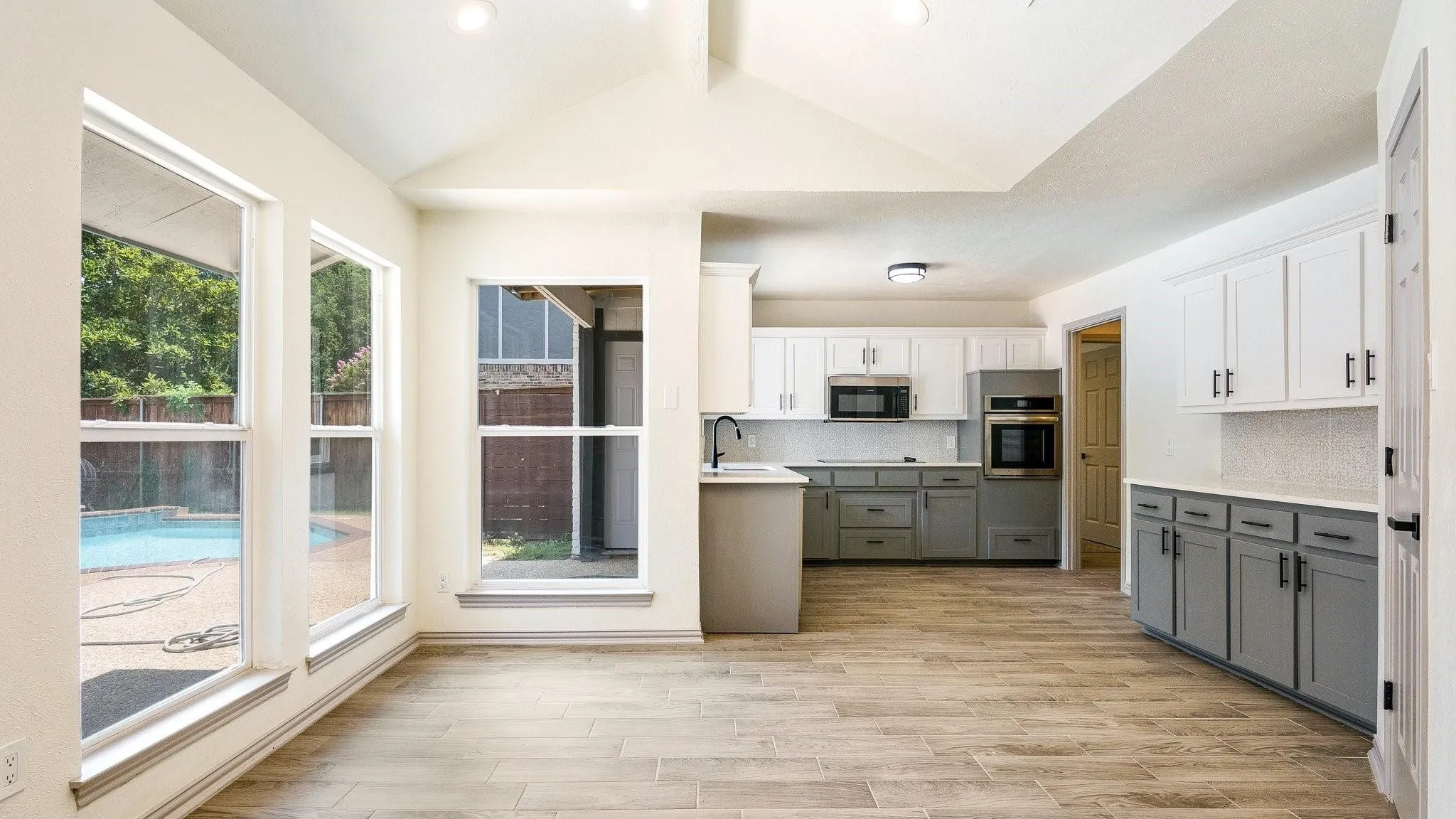 Wood-finish flooring, vaulted ceiling, two-tone cabinetry, stainless steel appliances, and a visible pool