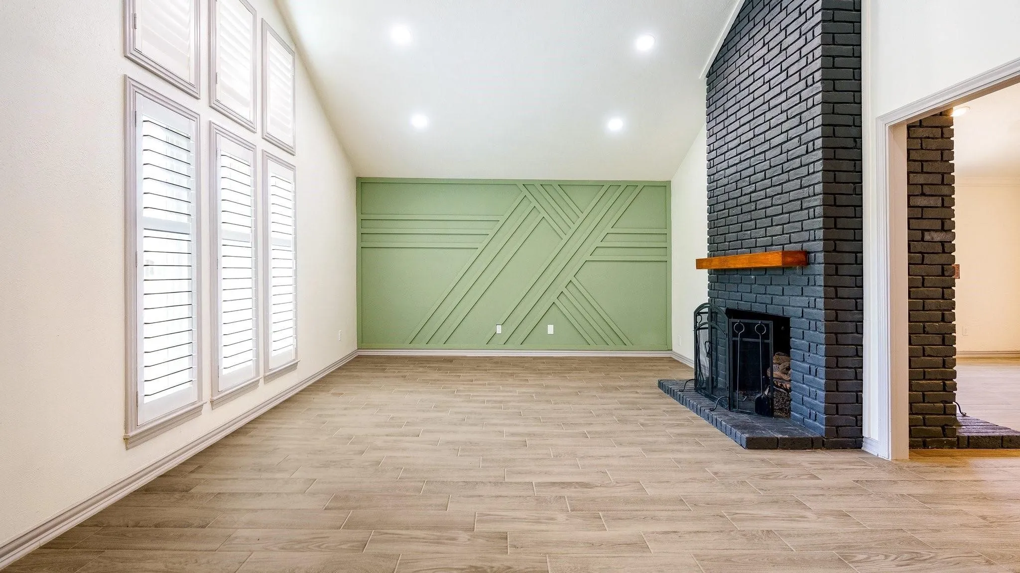 Vaulted ceiling with recessed lighting, wood-finish flooring, accent wall with decorative molding, and a black brick fireplace with a wood mantel