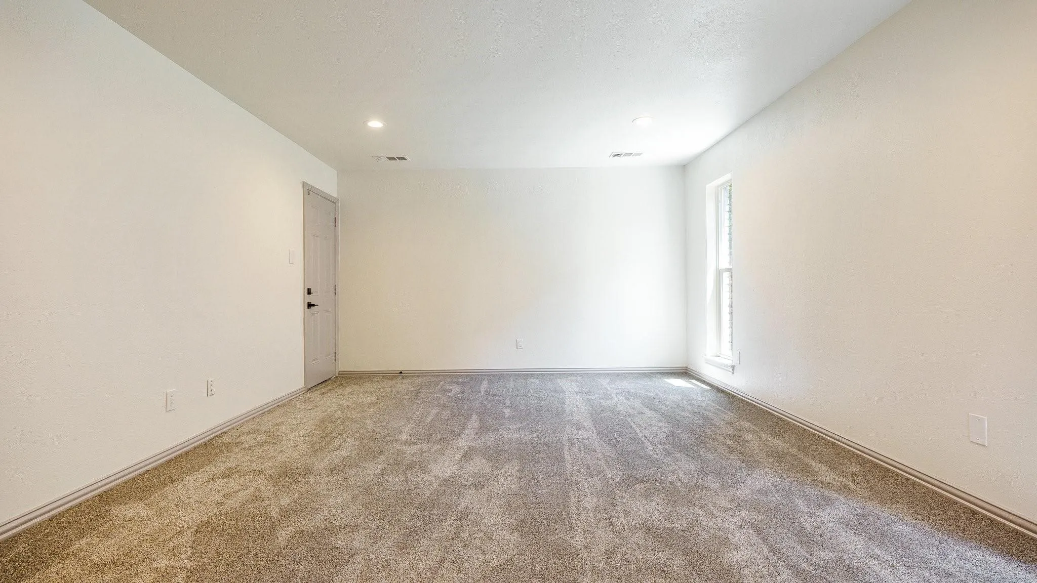 Textured carpet flooring, white painted walls, recessed ceiling lighting, and a single window