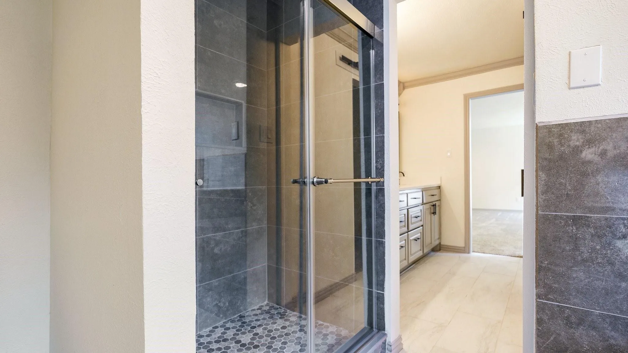 Glass-enclosed shower with gray tiled walls and a hexagonal mosaic tile floor