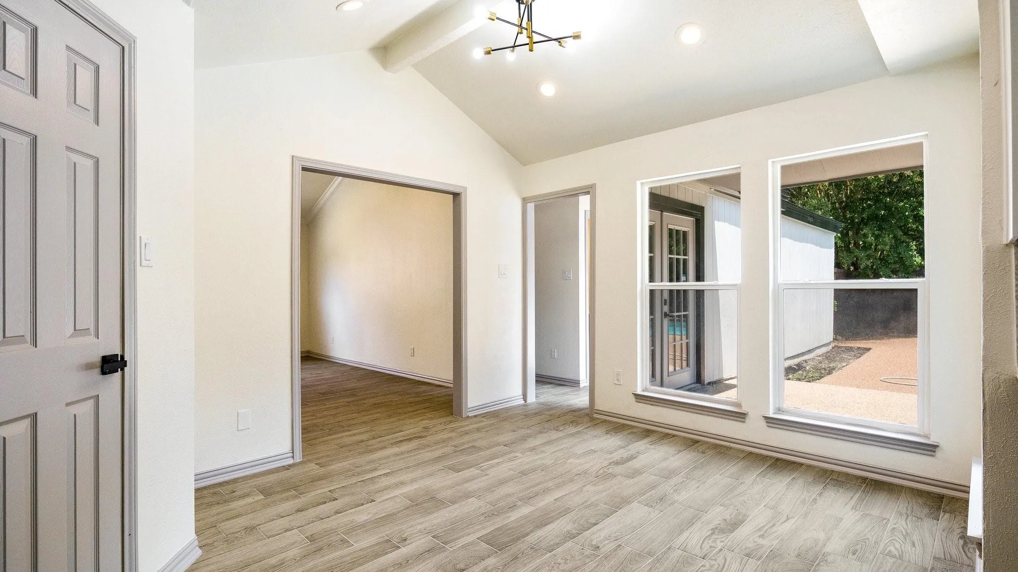 Vaulted ceiling with exposed beam, wood-finish flooring, recessed lighting, modern chandelier, and multiple windows