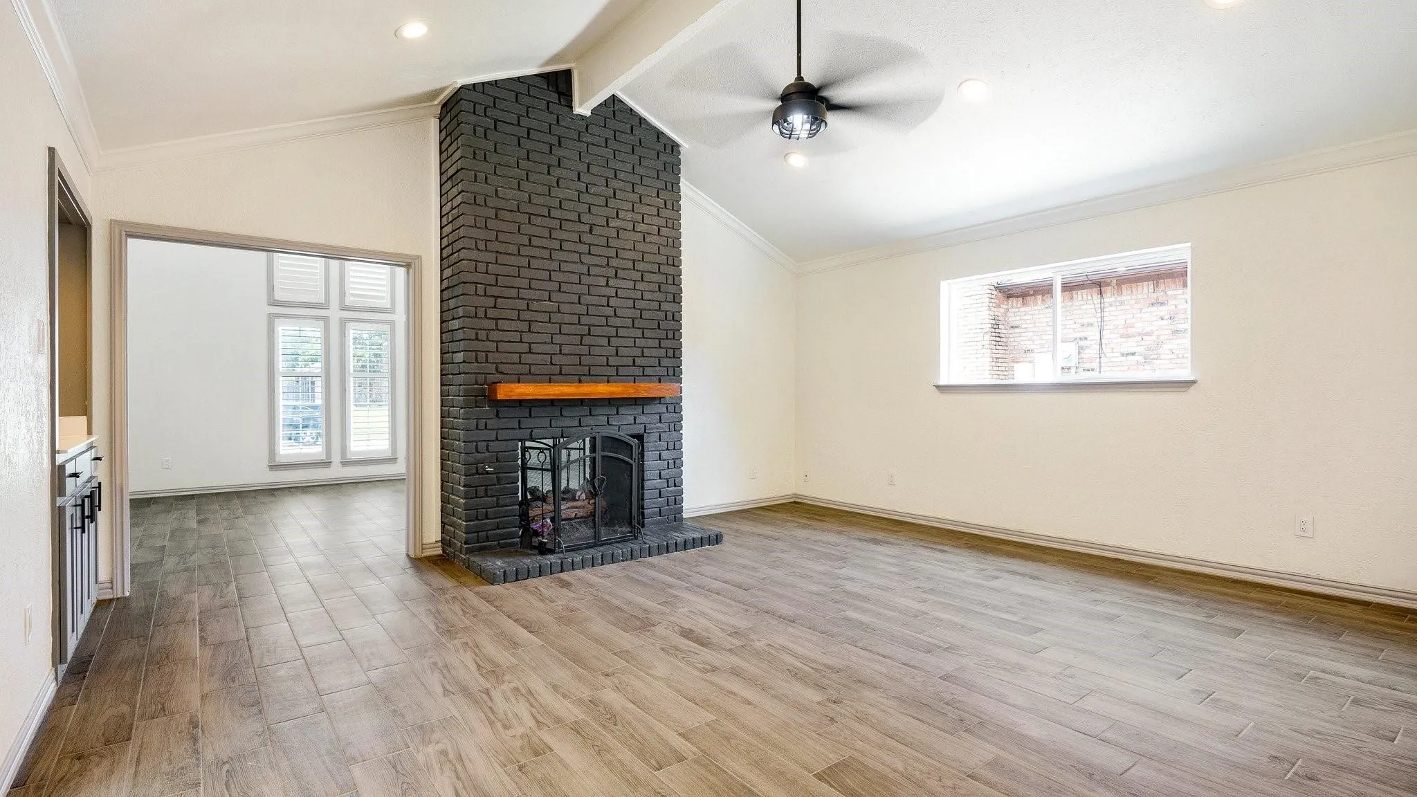 Vaulted ceiling, wood-finish flooring, black brick fireplace with wood mantel, recessed lighting, and ceiling fan