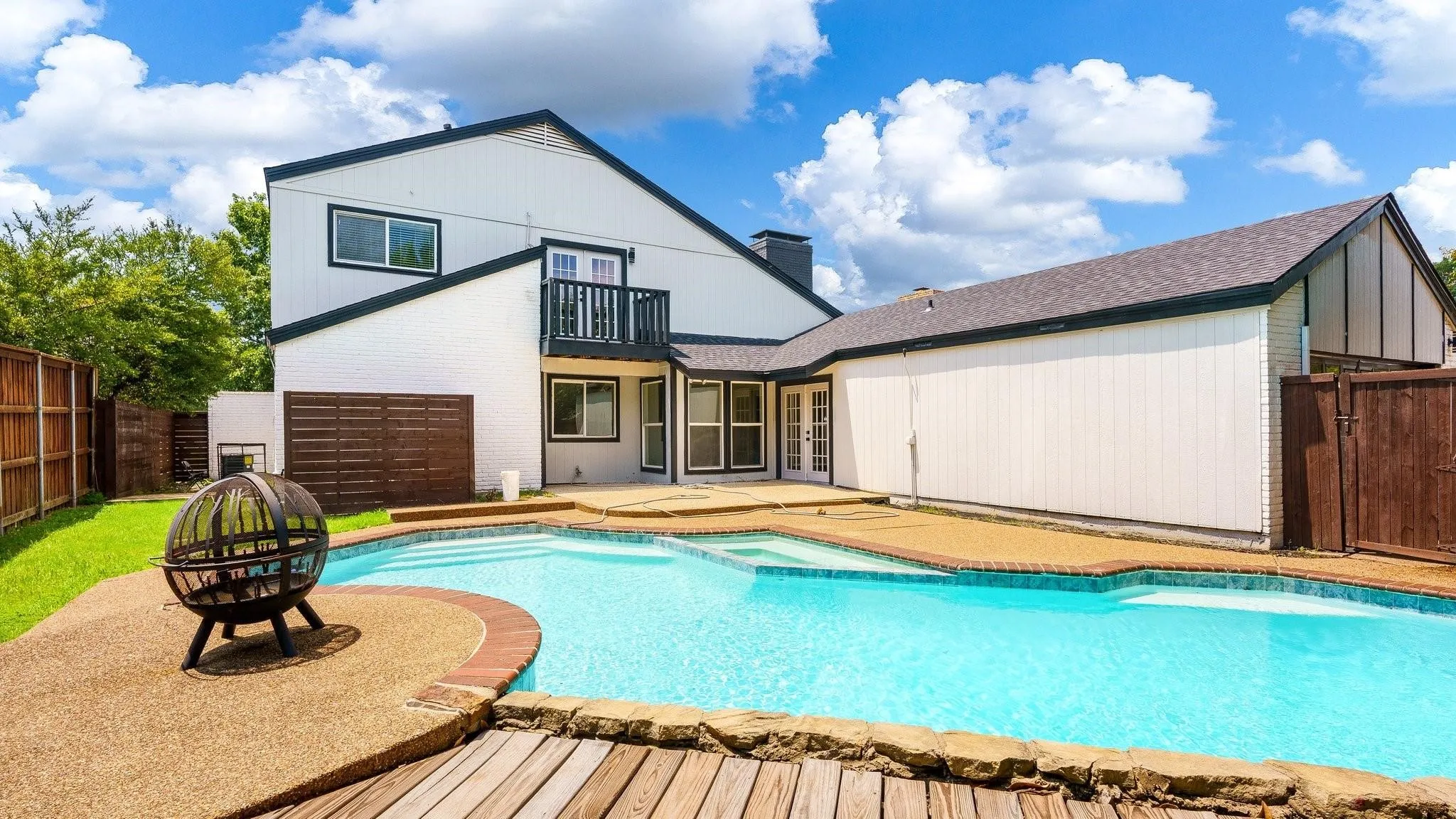 Expansive backyard with a built-in swimming pool, surrounding aggregate and wood-finish decking, and a privacy fence