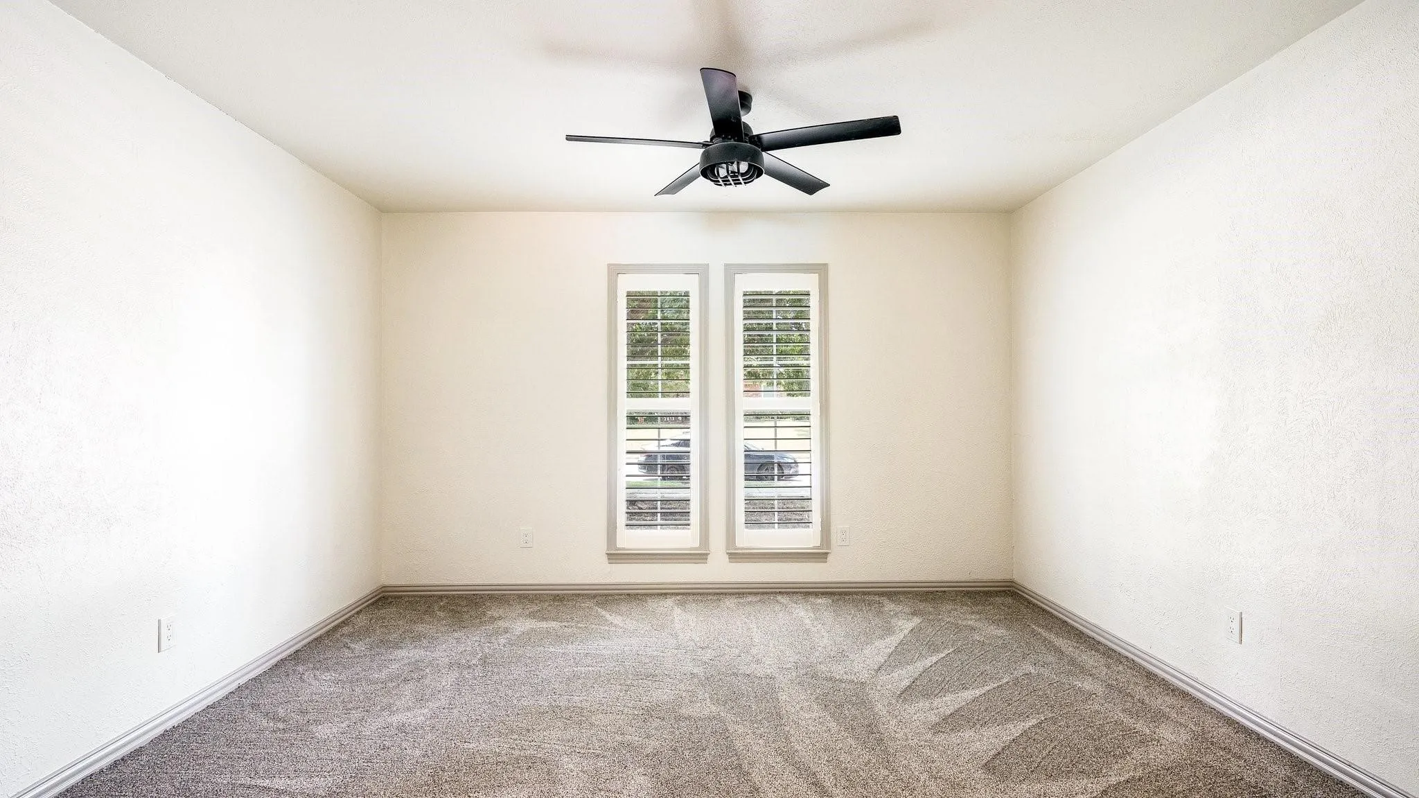 Neutral wall color, carpeted flooring, two windows with plantation shutters, ceiling fan with integrated lighting, and crown molding