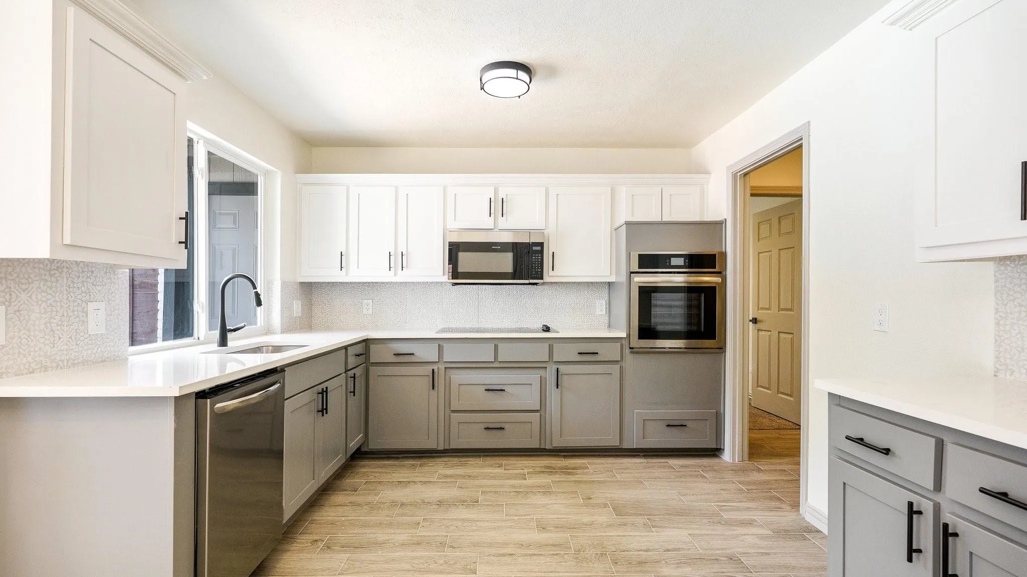 Modern kitchen featuring two-tone cabinetry, stainless steel appliances, white countertops, a mosaic tile backsplash, and wood-finish flooring