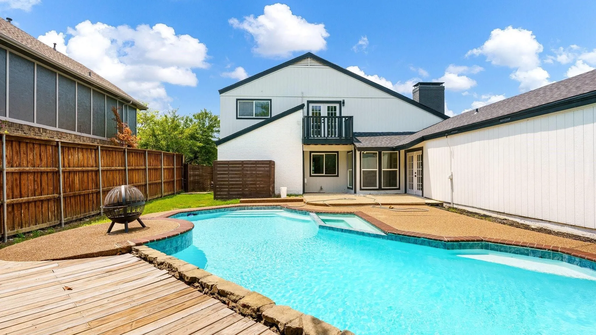 Outdoor living space featuring a swimming pool with integrated spa, wood decking, and an elevated balcony with railing