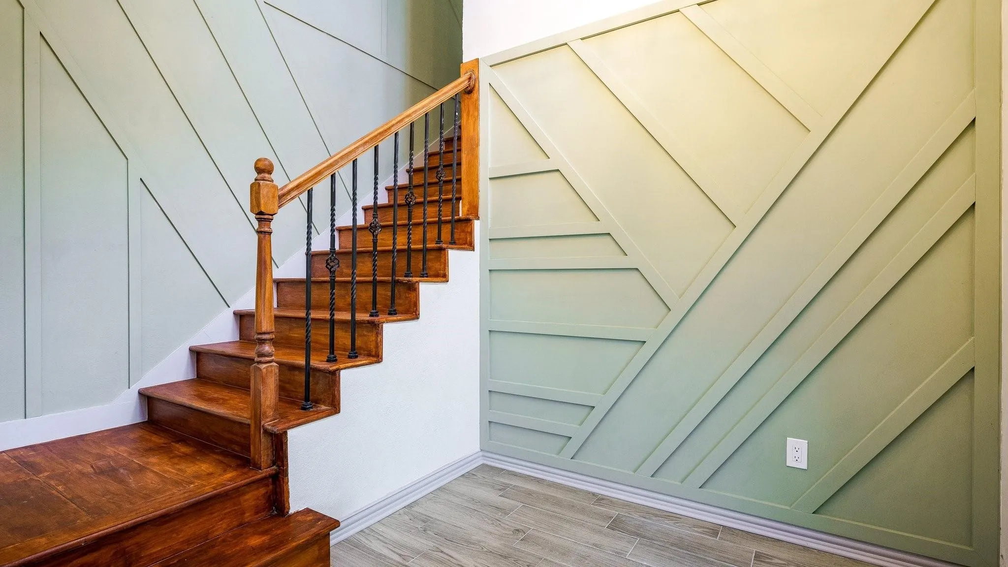 Hardwood staircase with decorative wrought iron balusters, custom geometric accent wall paneling, and wood-finish tile flooring