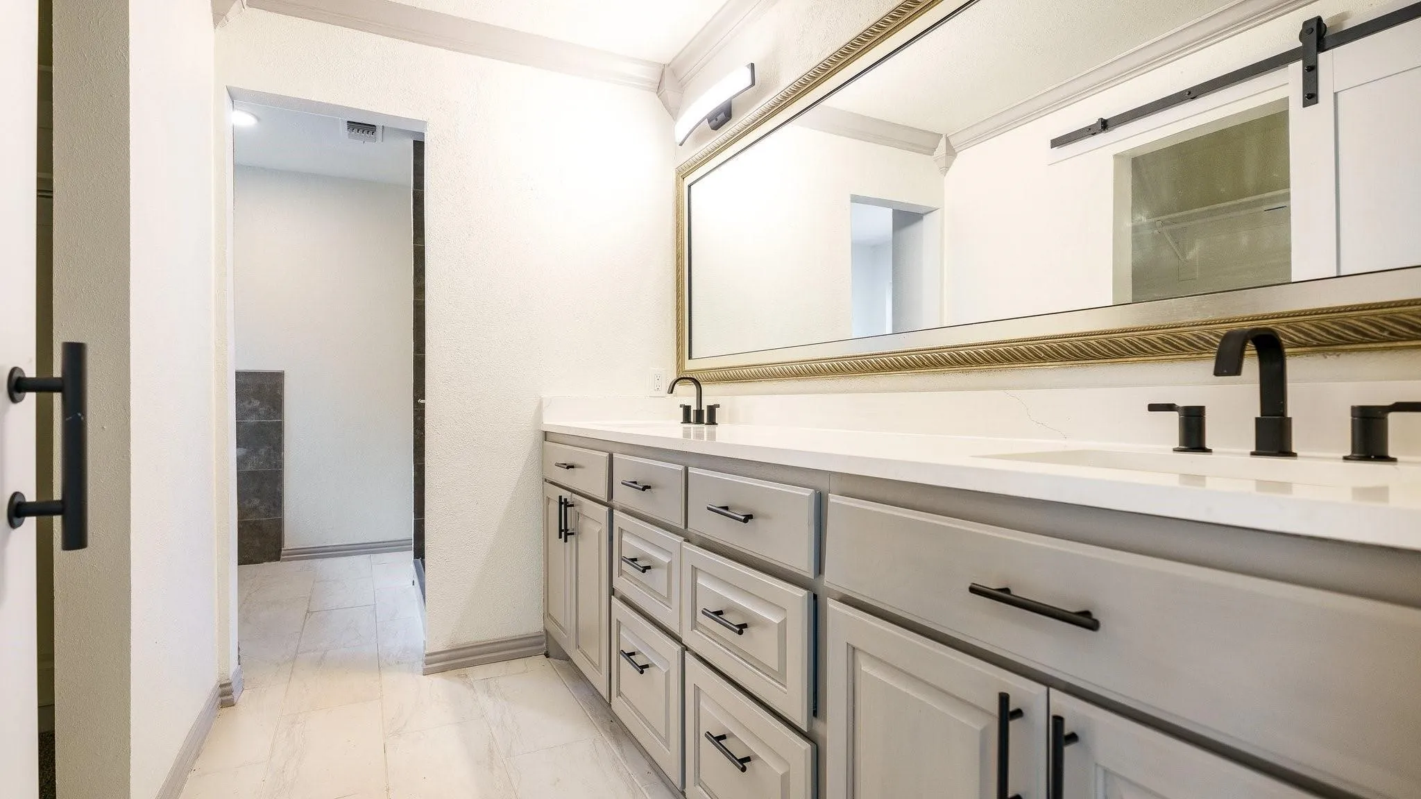 Dual vanity with matte black fixtures, light-toned cabinetry, and a large wall-mounted mirror