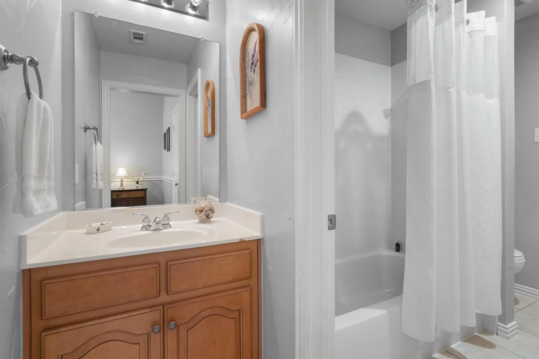 Bathroom featuring a wood-finish vanity with a built-in sink, a wall-mounted mirror, and a bathtub with a shower